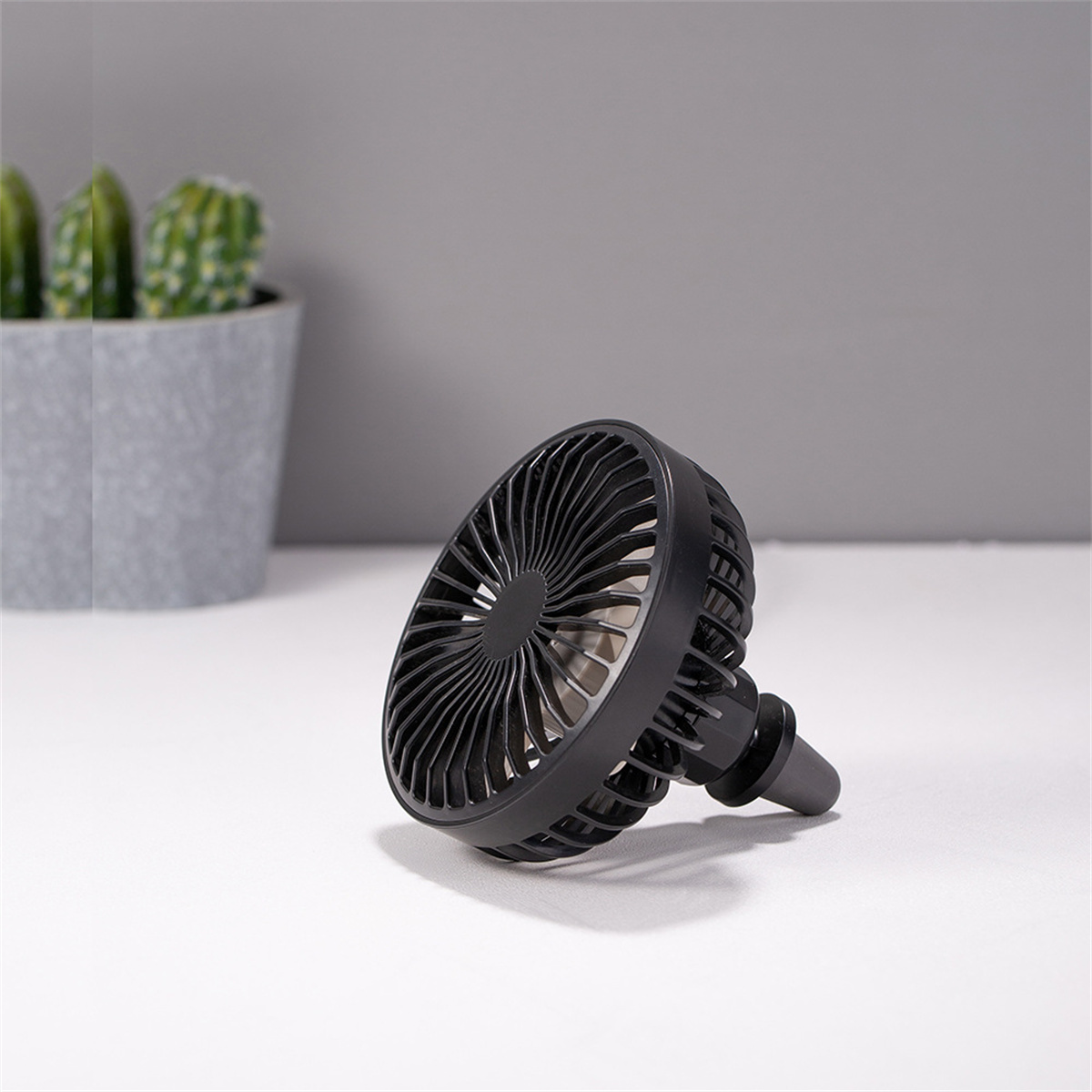 Ventilador negro sobre una superficie blanca, en ángulo hacia el espectador, con un fondo gris.