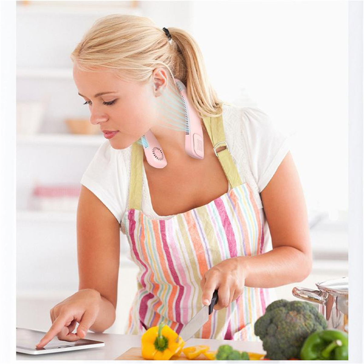 Mujer en la cocina con un ventilador de cuello. Corta verduras en una tabla de cortar.