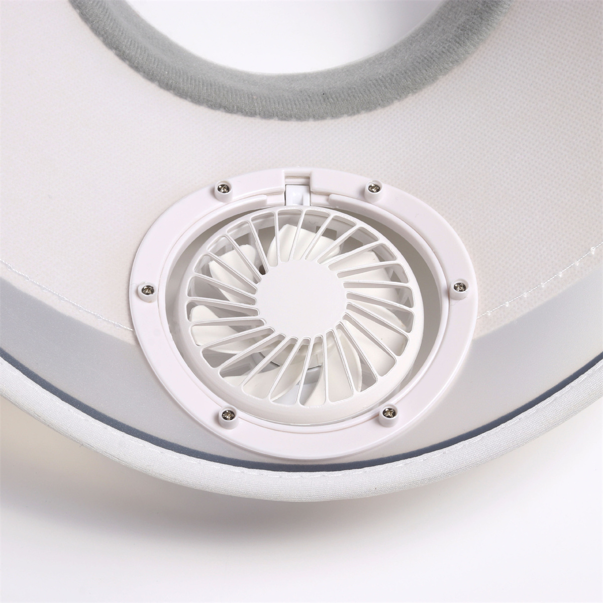 Una vista de cerca de un pequeño ventilador incorporado en un sombrero para el sol blanco, con detalles blancos y grises.