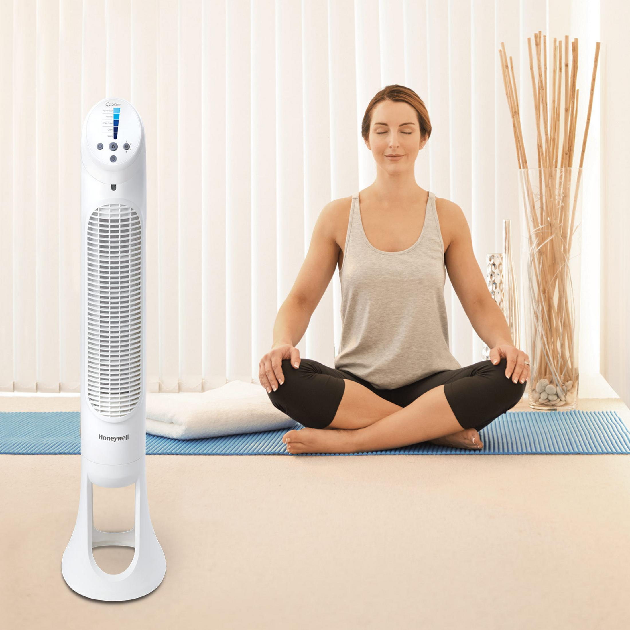 Eine Frau meditiert, links ein weißer Ventilator.