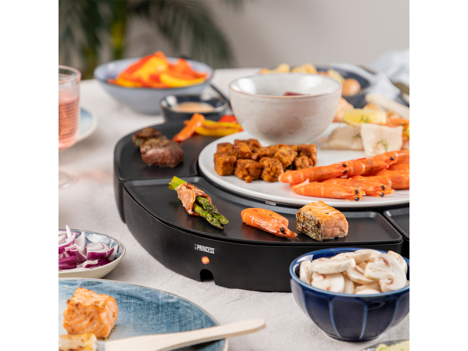 Ein Tisch mit einem schwarzen Grill. Es gibt verschiedene Speisen darauf, wie Garnelen, Steak und Gemüse.