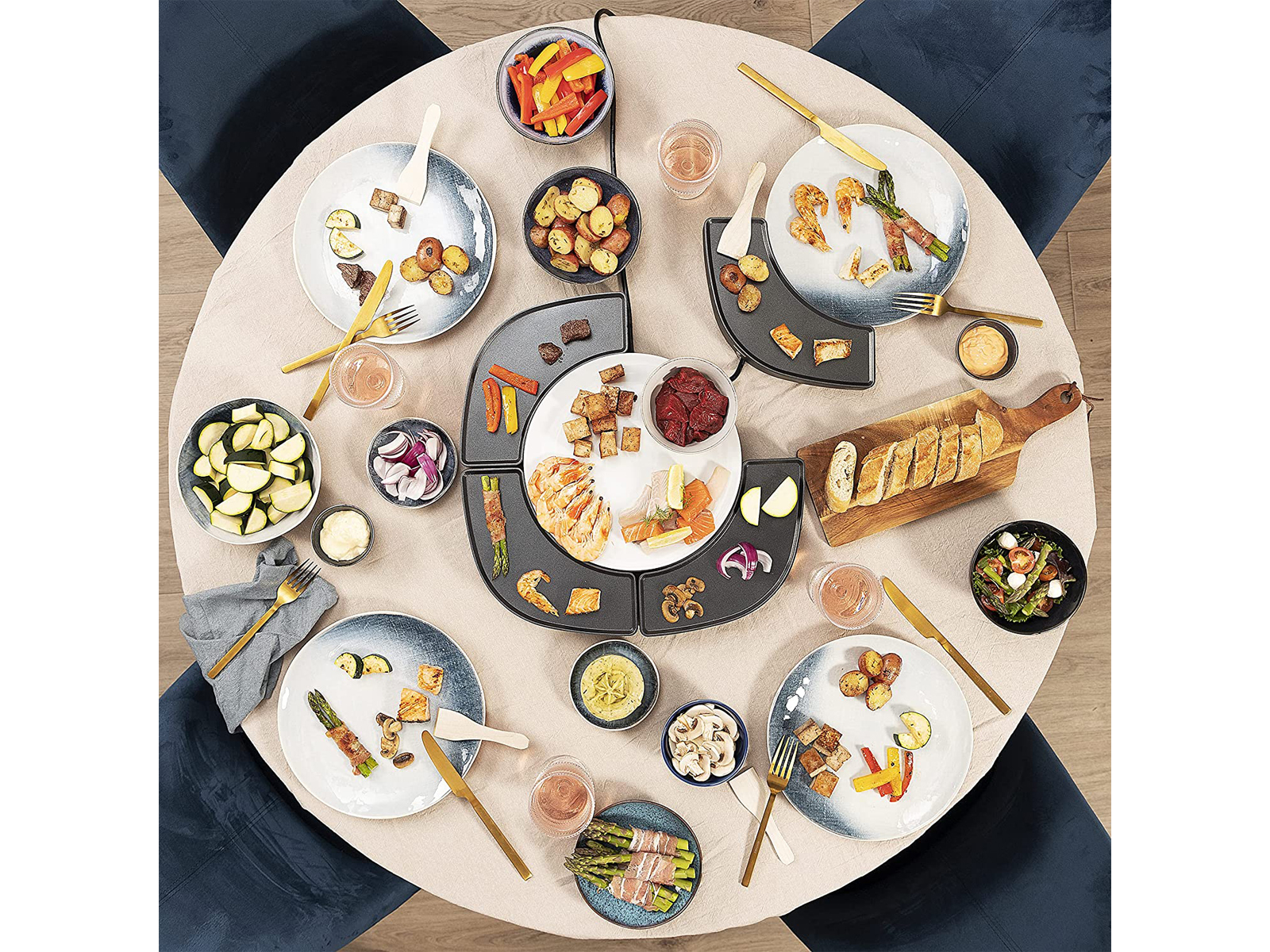 Ein Tisch für ein Fondue-Essen. Enthält Teller mit Essen, Saucen und ein zentrales Kochfeld.