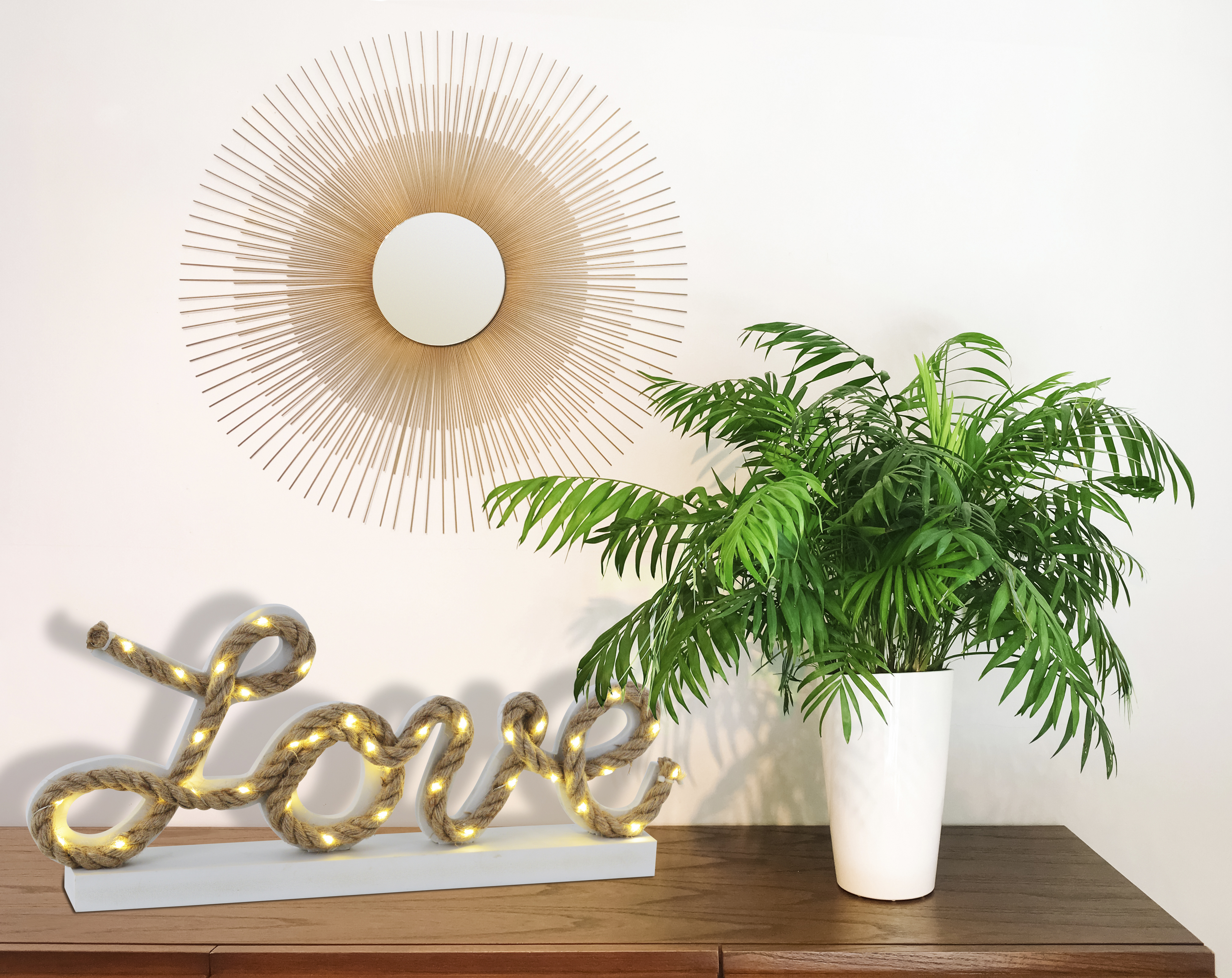 Wand mit goldenem Sonnenstrahlspiegel, „Love“-Schild und einer Topfpflanze.