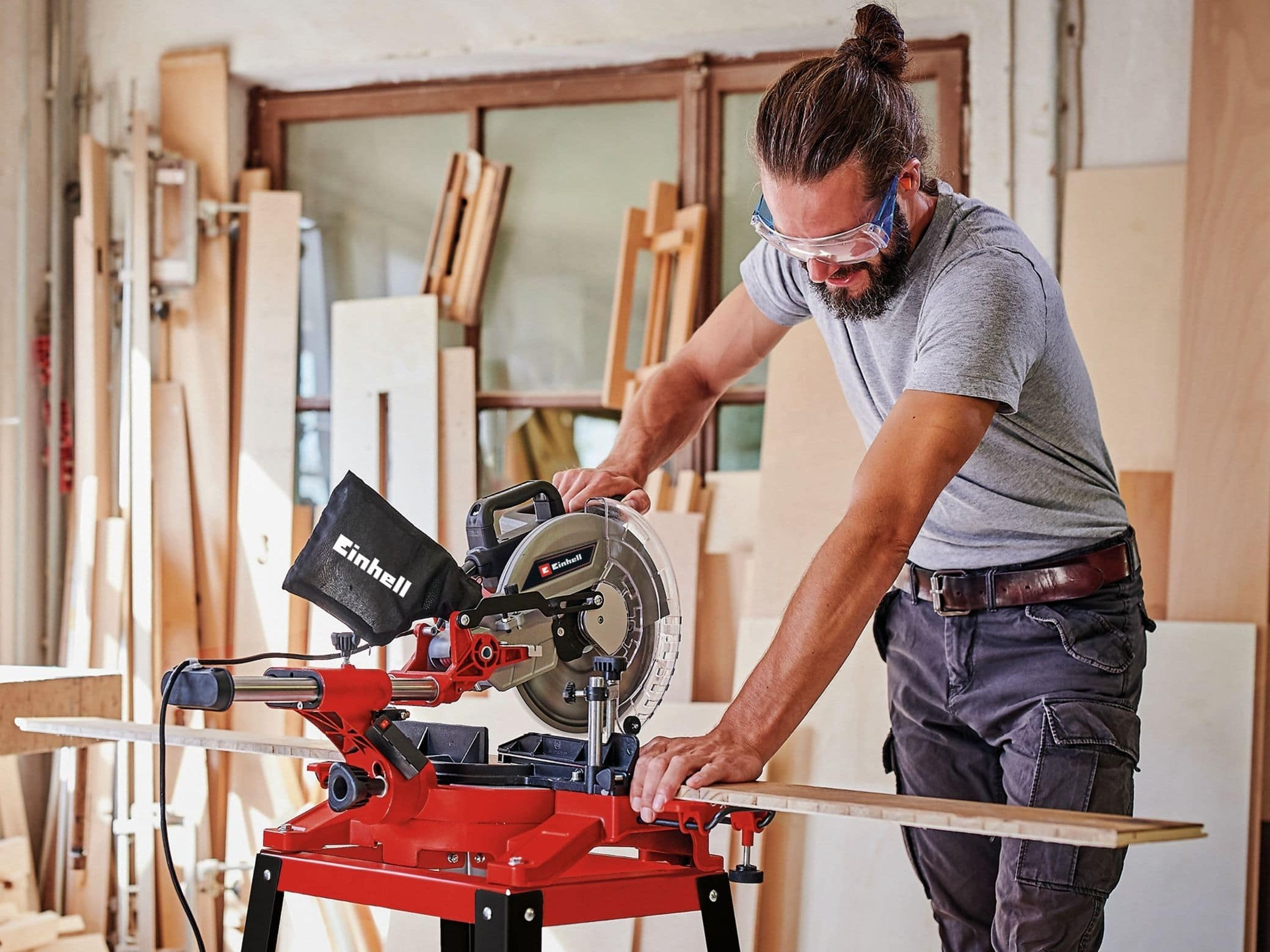 Ein Mann mit Schutzbrille schneidet mit einer roten Säge eine Holzbohle.