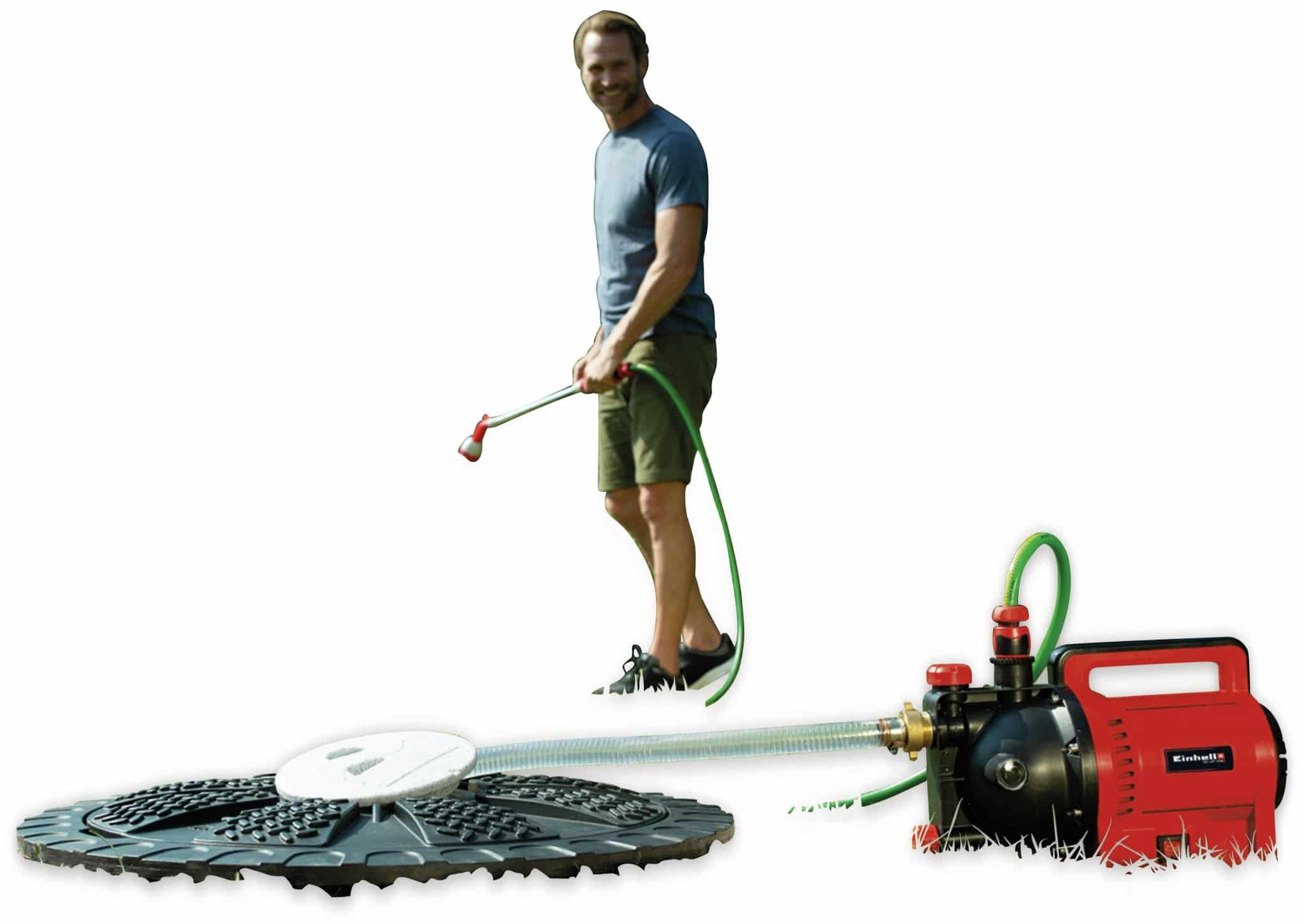 Mężczyzna podlewający trawę wężem. Pompa i zraszacz na pierwszym planie.