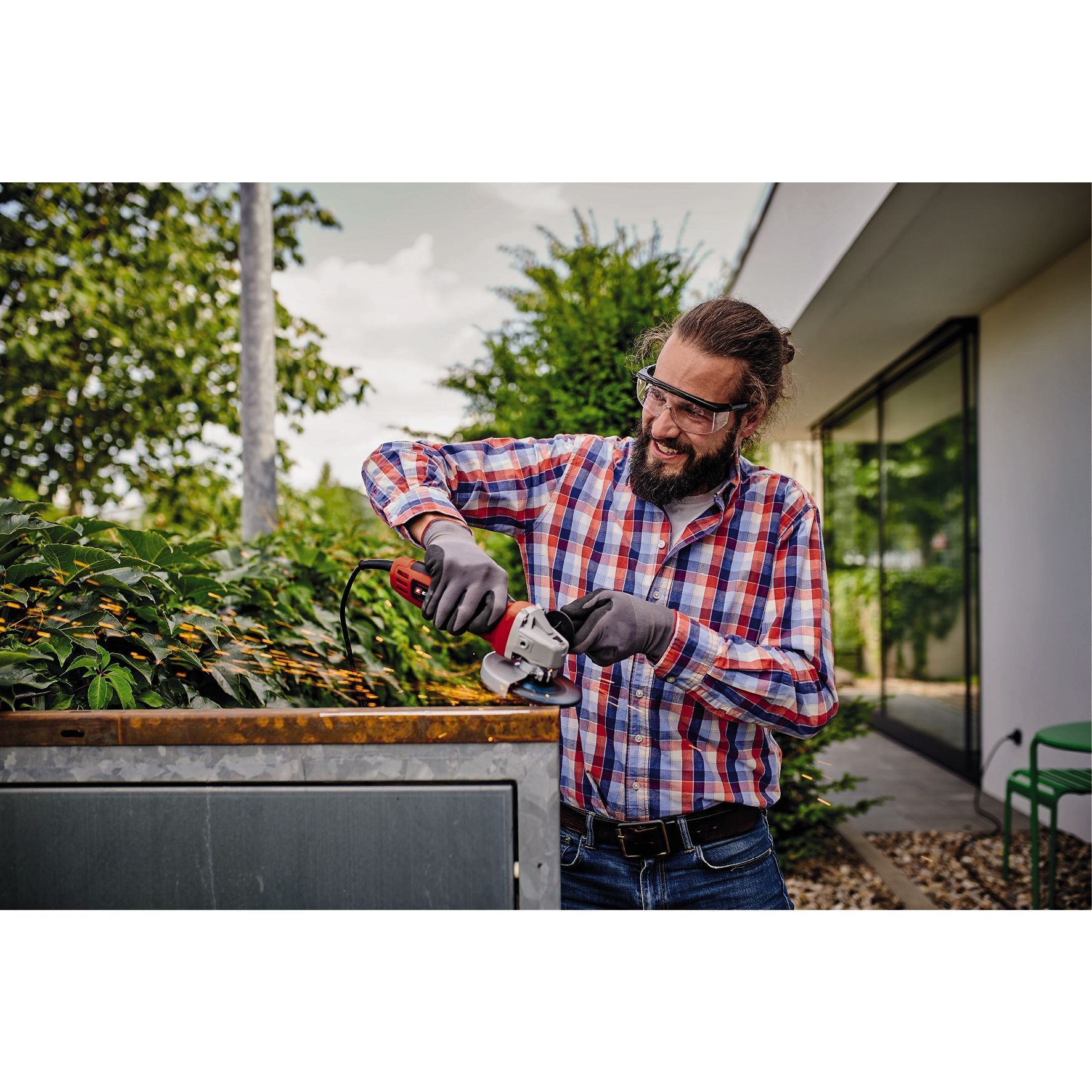 Mężczyzna używający szlifierki kątowej, noszący okulary ochronne, na zewnątrz.