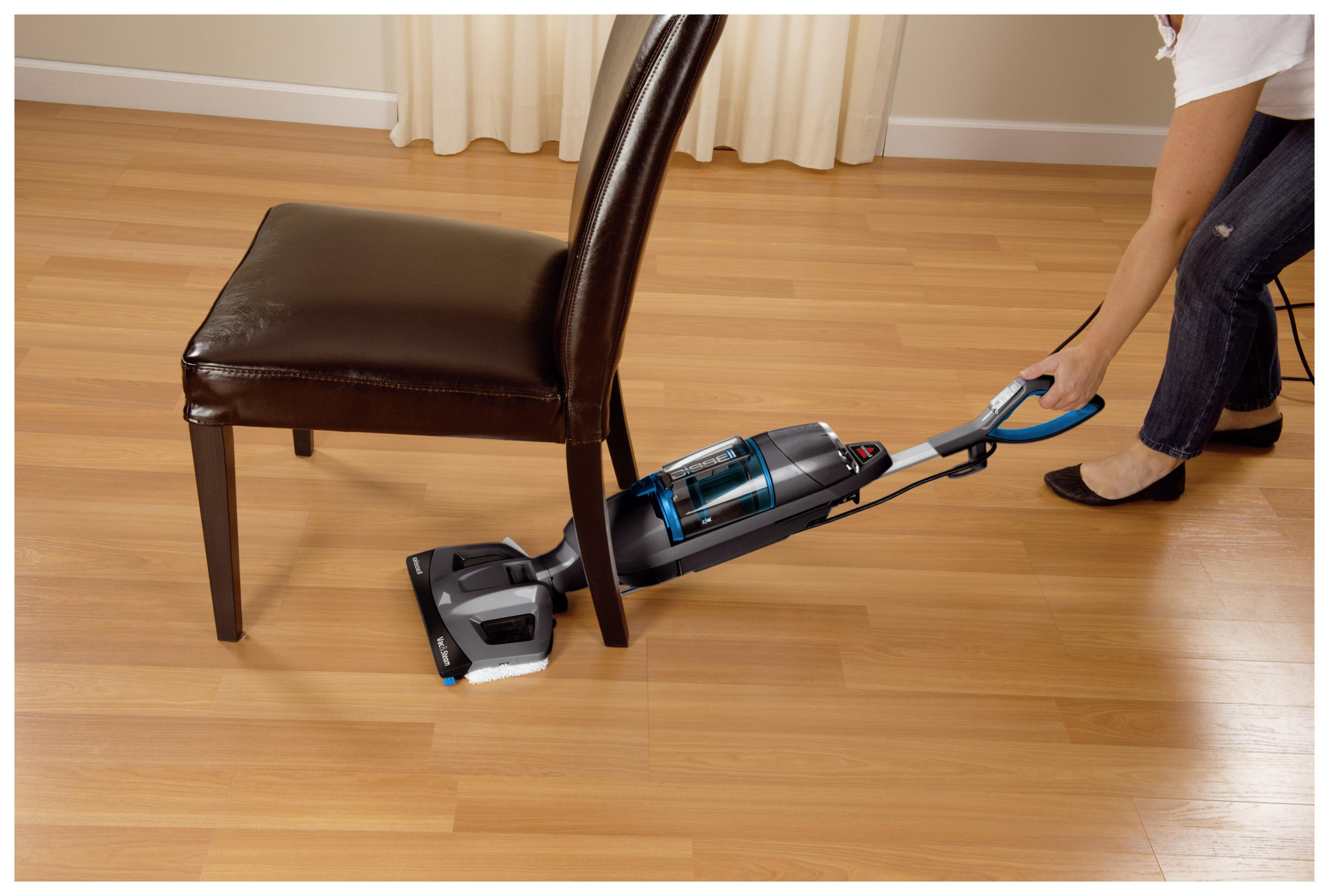Osoba używająca odkurzacza wokół krzesła na drewnianej podłodze.