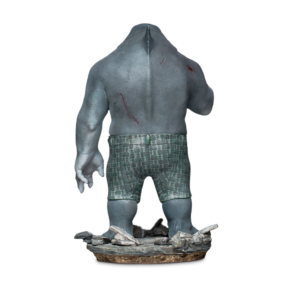 Haifisch-ähnliche Kreaturenstatue von hinten, trägt Shorts und steht auf Sockel.