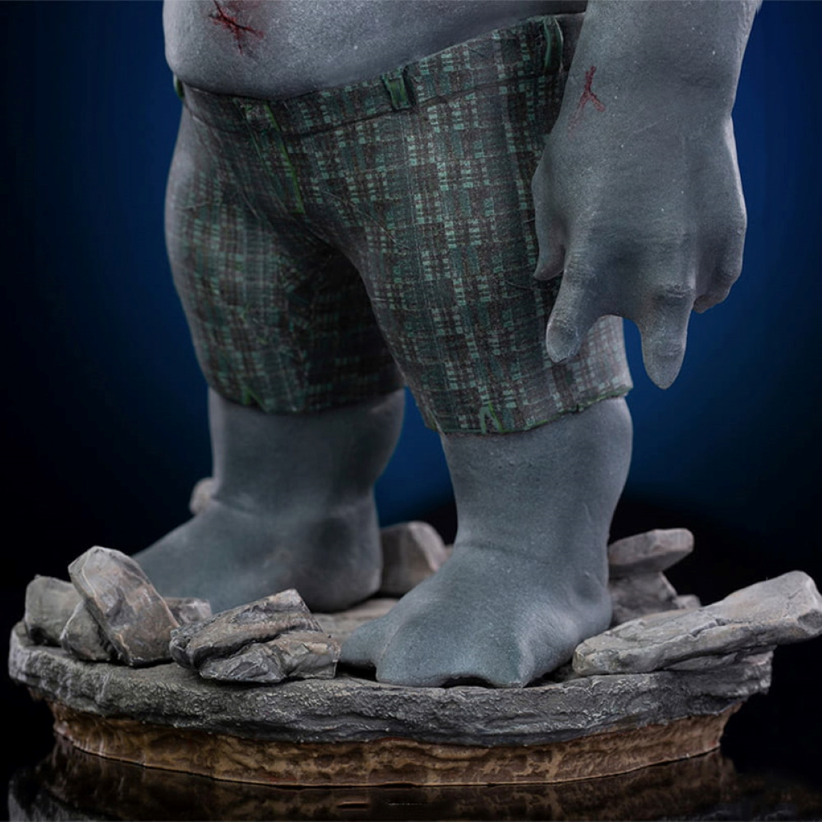 Statue einer grauen, humanoiden Figur mit kurzer Hose und sichtbaren Wunden.