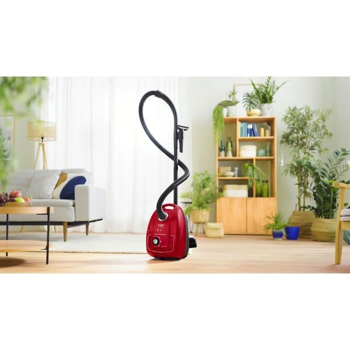 Aspiradora roja con manguera negra en sala de estar con muebles y plantas.