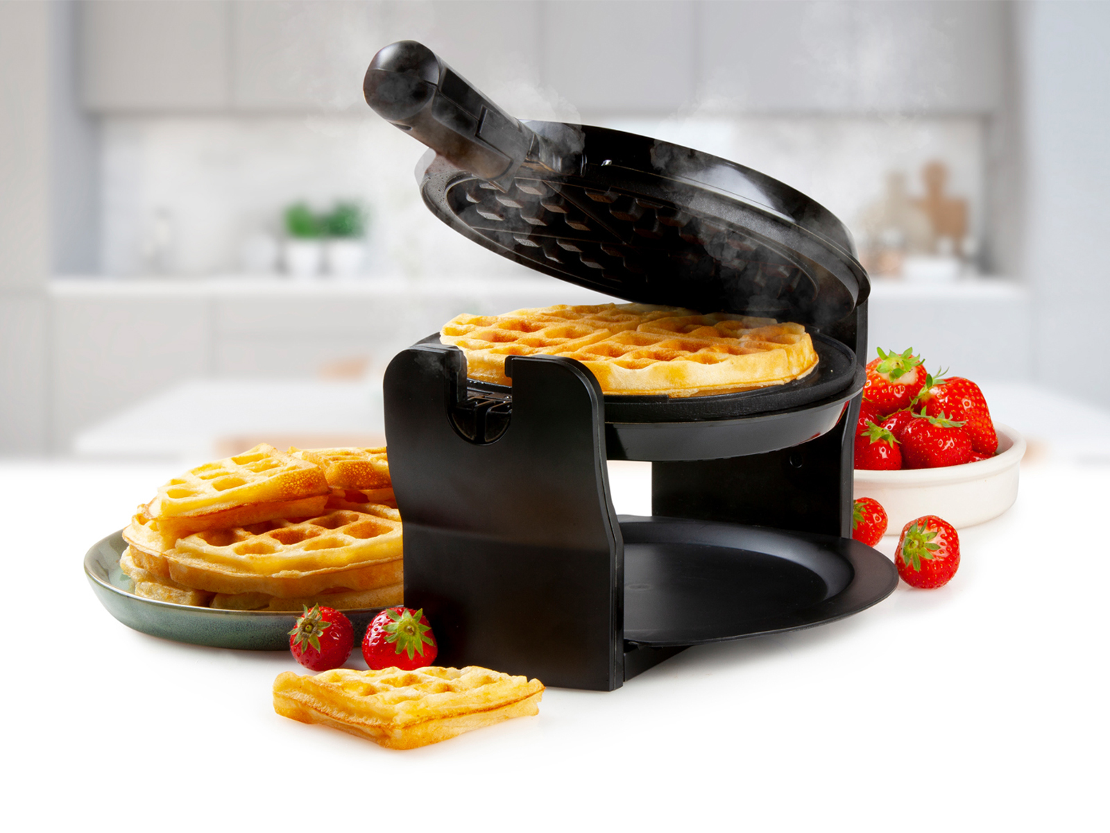 Waffeleisen mit Waffeln. Waffeln auf einem Teller gestapelt, Erdbeeren daneben.