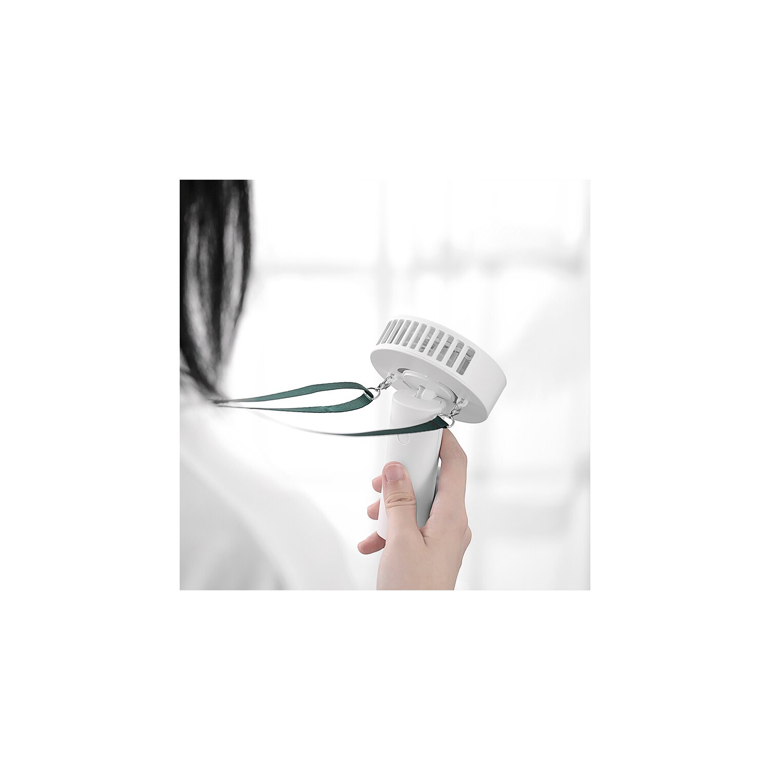 Eine Person hält einen kleinen, weißen Handventilator. Der Ventilator hat einen grünen Riemen.