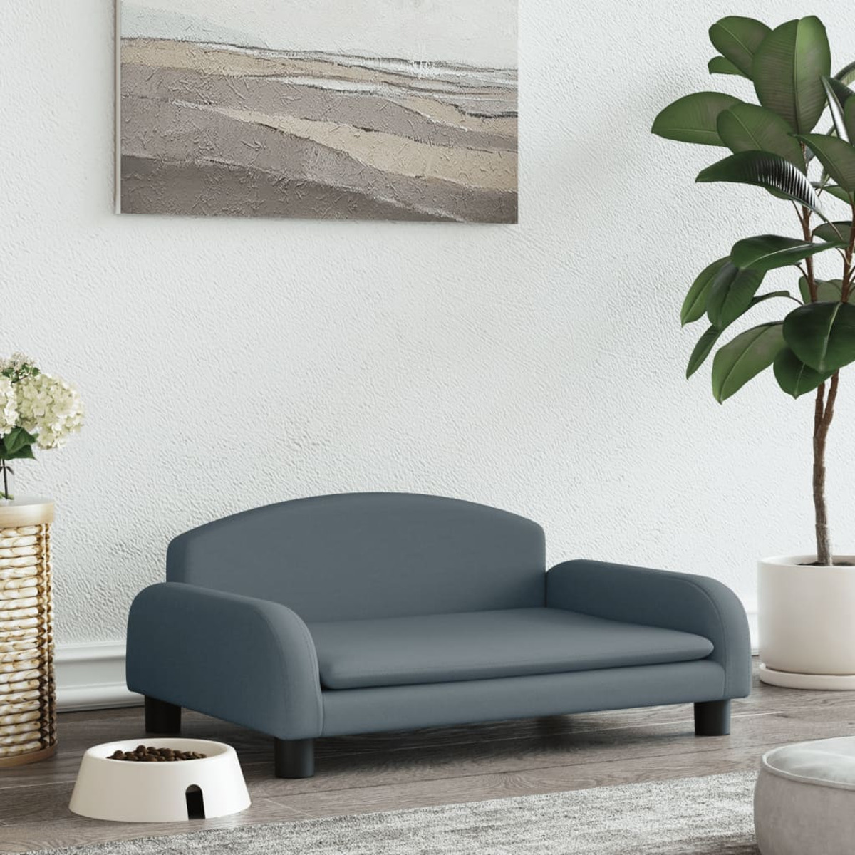 Graues Hundebett. Blaues Kissen, weiße Schüssel mit Futter, Gemälde und eine Topfpflanze. Weiße Wand.