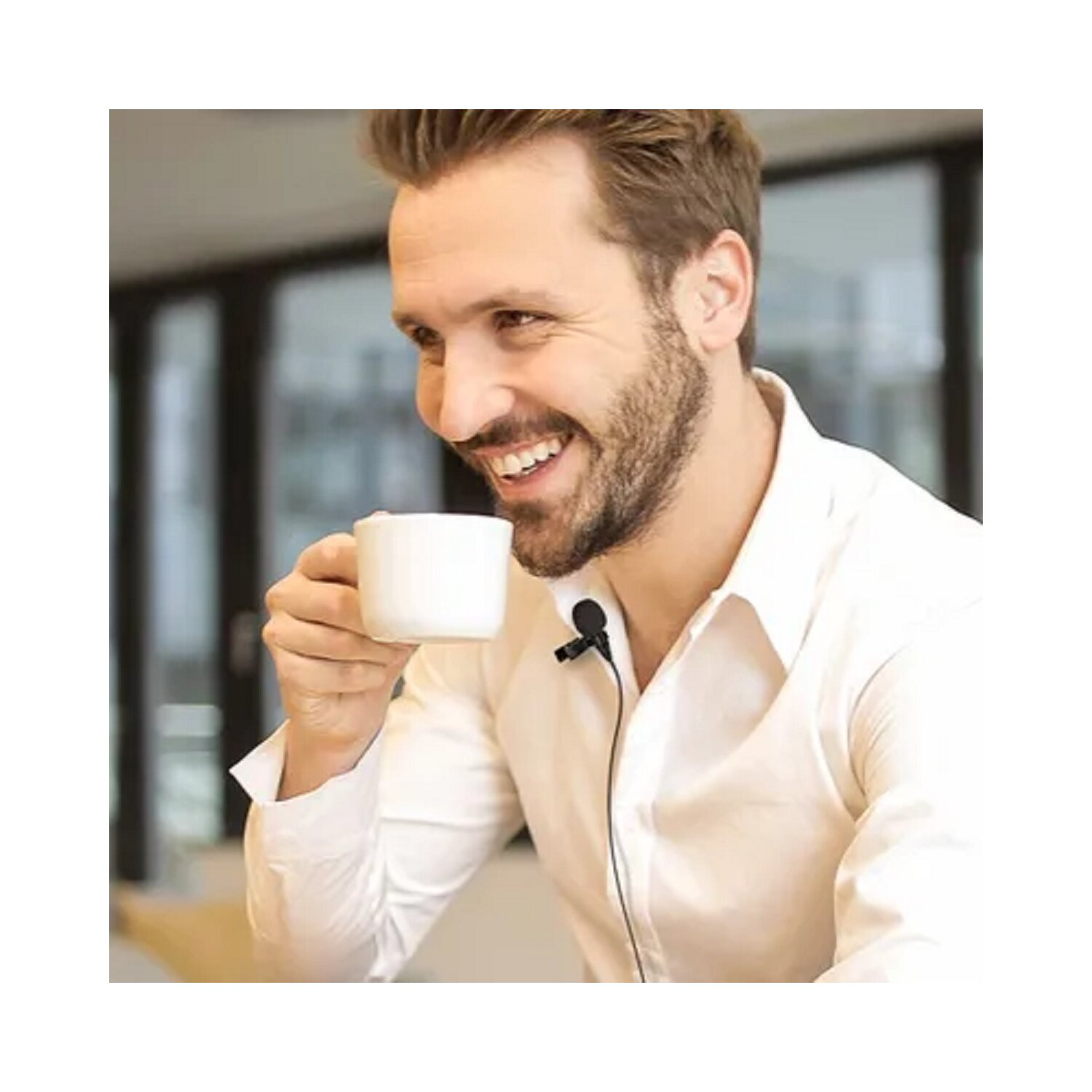 Mann lächelt, hält eine weiße Tasse. Er trägt ein weißes Hemd und hat ein Lavalier-Mikrofon.
