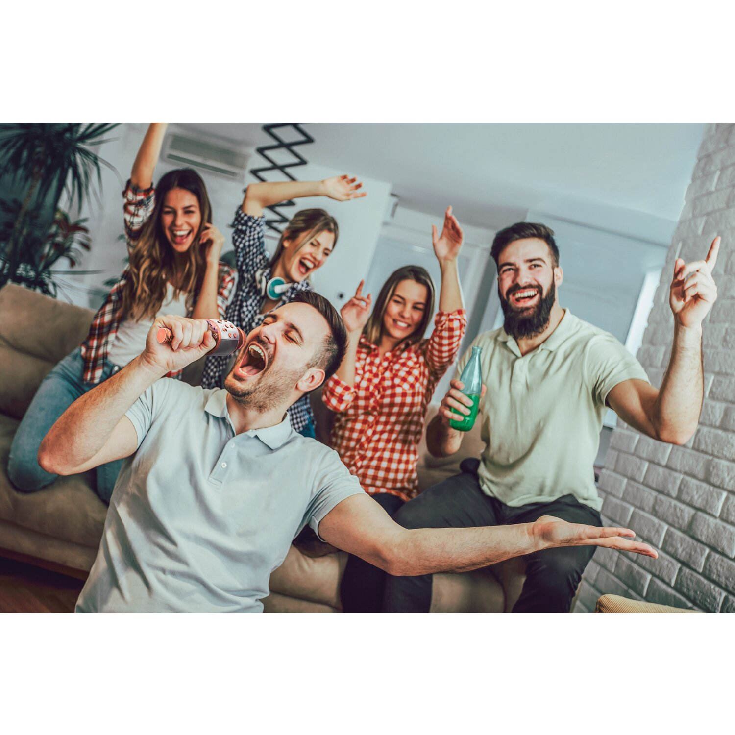 Freunde singen Karaoke. Ein Mann singt ins Mikro, andere tanzen, lächeln, drinnen.