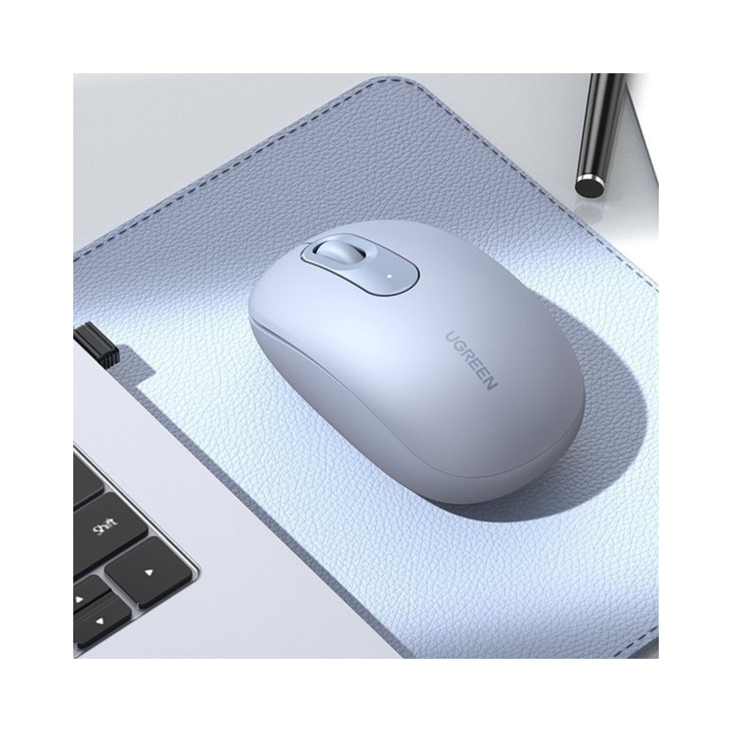 Jasnoniebieska mysz UGREEN na niebieskiej podkładce, obok laptopa. Mysz ma kółko przewijania i logo UGREEN.