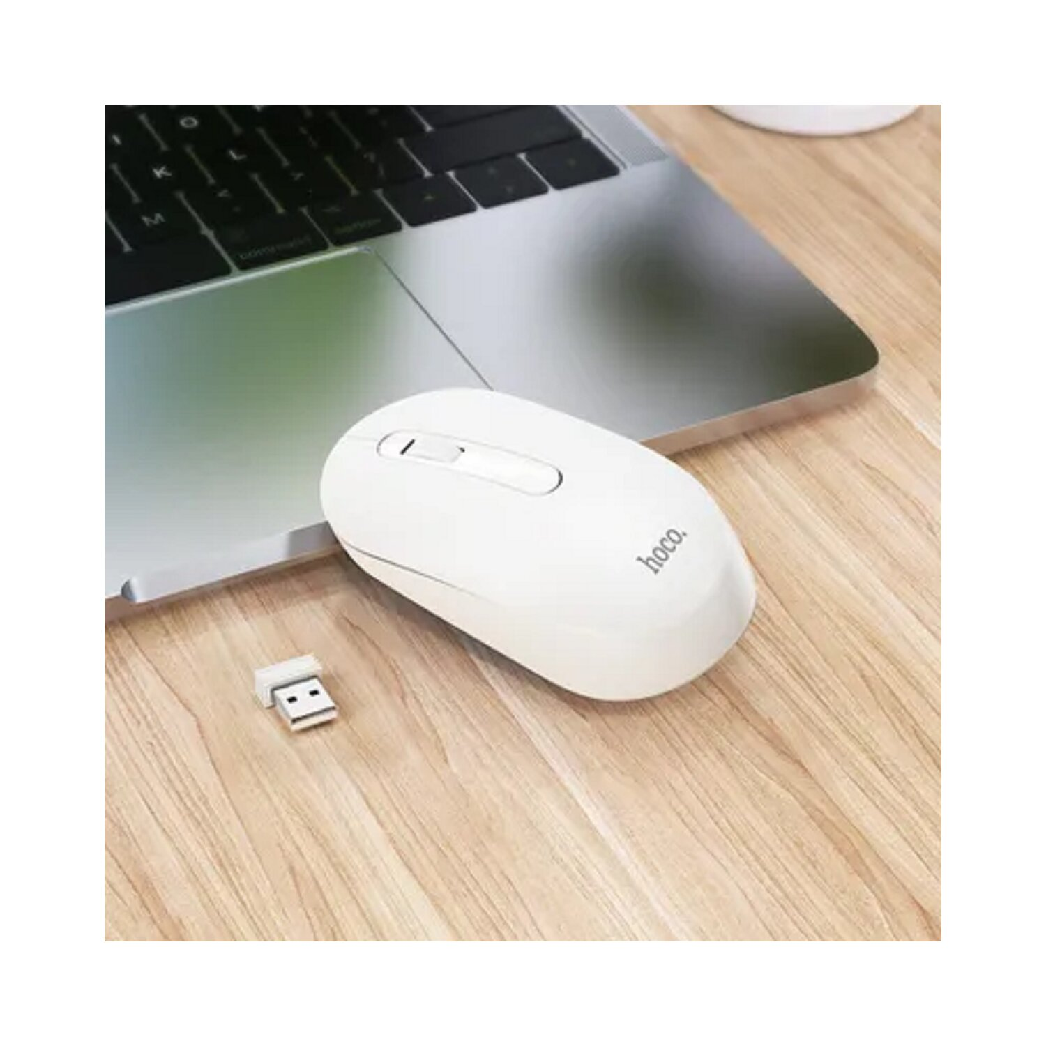 Ratón inalámbrico blanco y su receptor USB sobre una superficie de madera, portátil parcialmente visible.