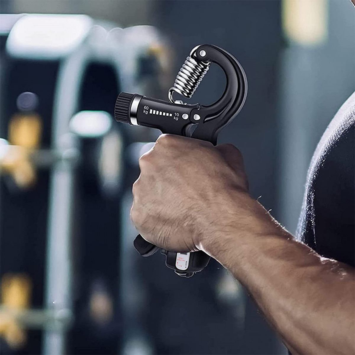 Mężczyzna trzyma czarny uchwyt do rąk, ściskając go. W tle widoczna siłownia.
