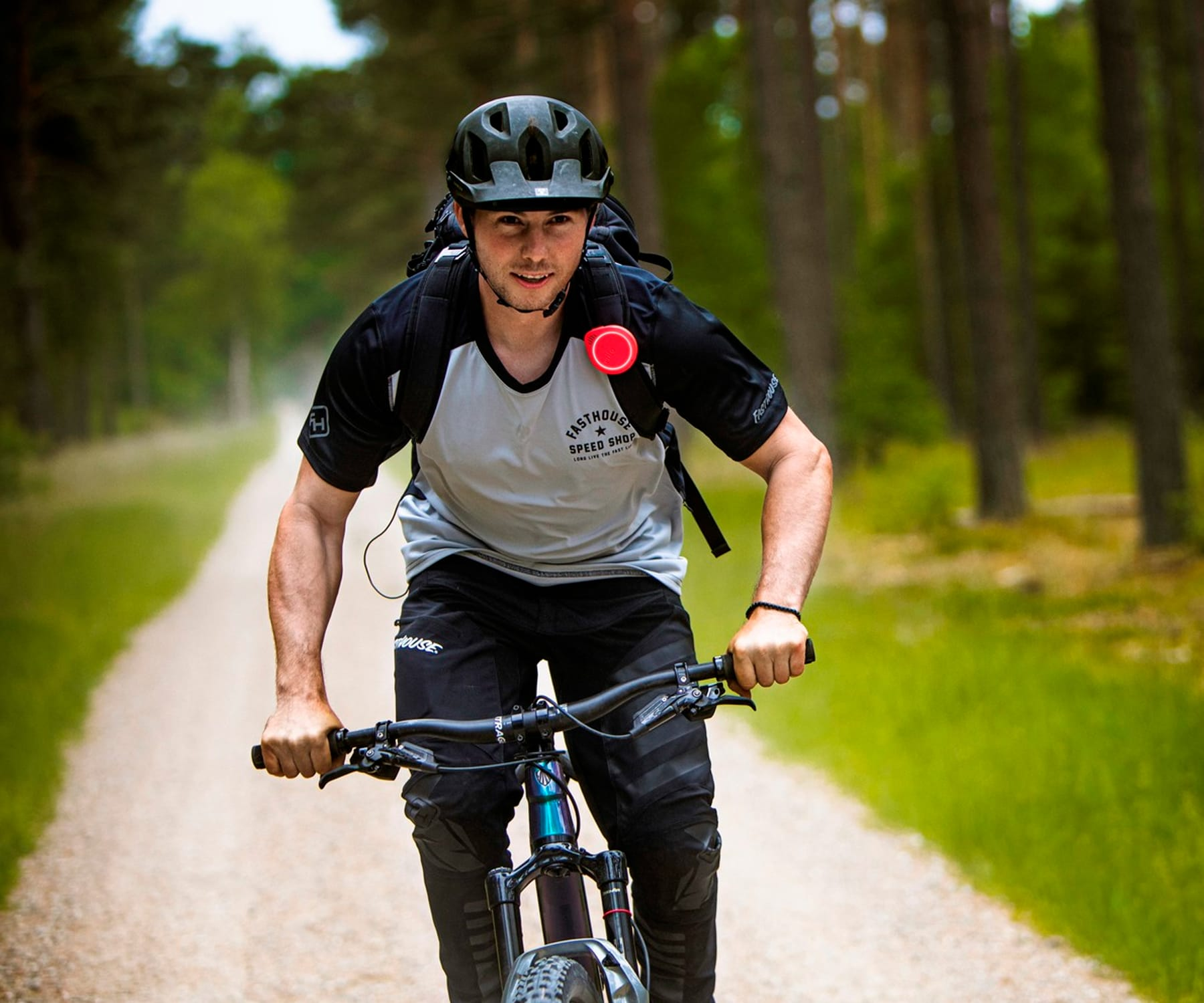 Un hombre monta en bicicleta de montaña por un camino de tierra en un bosque. Usa casco y mochila.