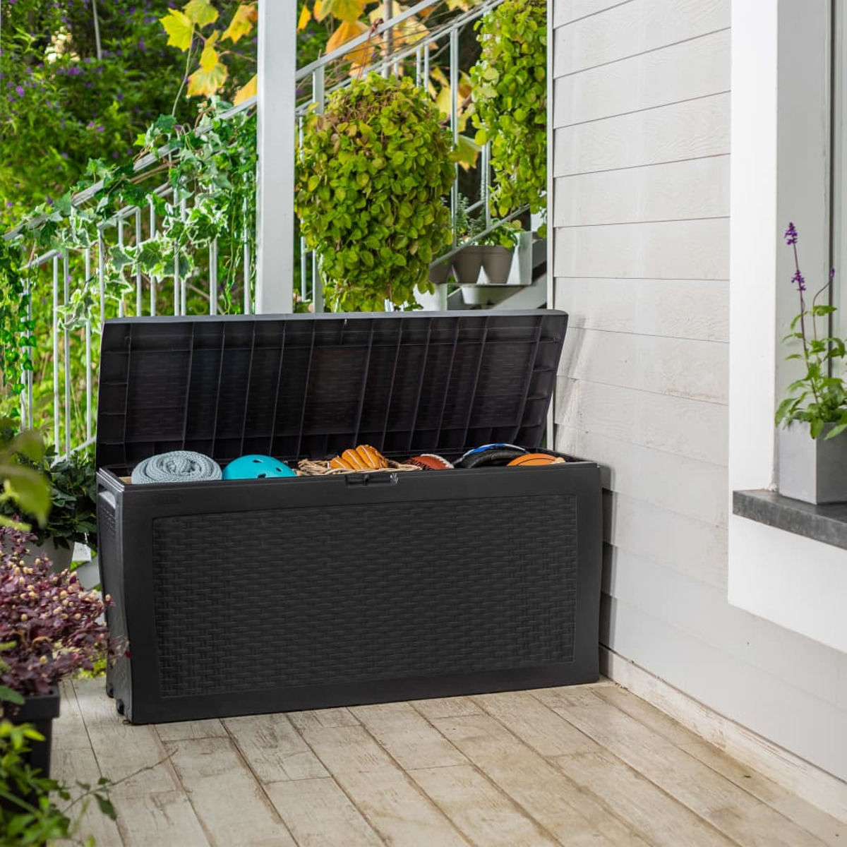 Schwarze Outdoor-Aufbewahrungsbox, offen, mit Gegenständen darin, auf einer Holzveranda.