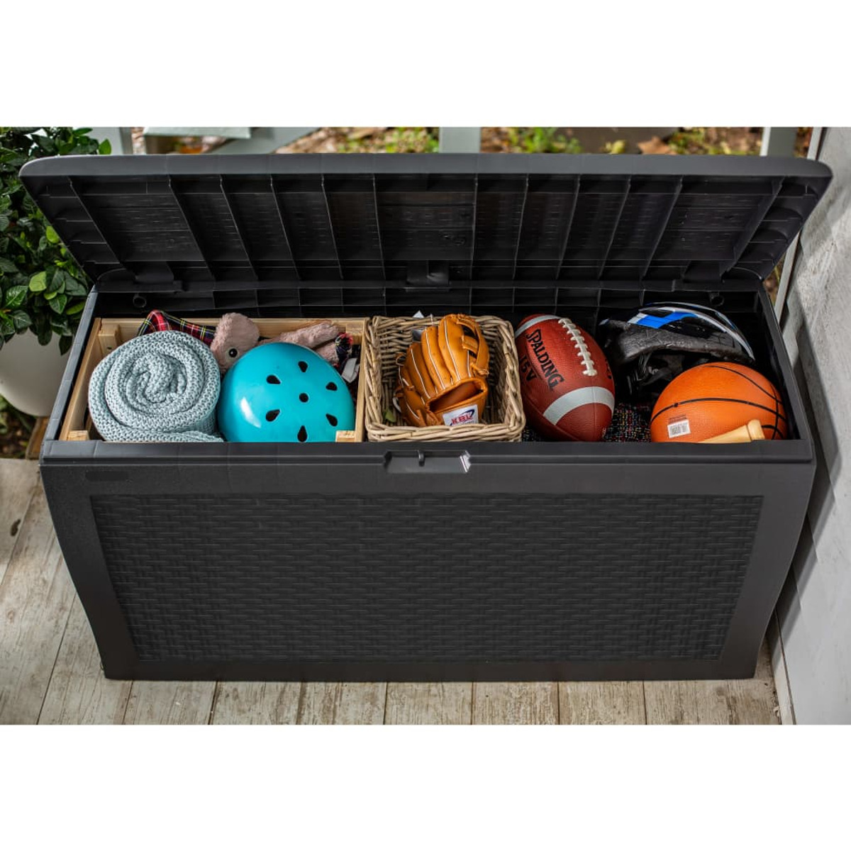 Eine große schwarze Aufbewahrungsbox gefüllt mit Gegenständen wie Spielzeug, Bällen und einer Decke.