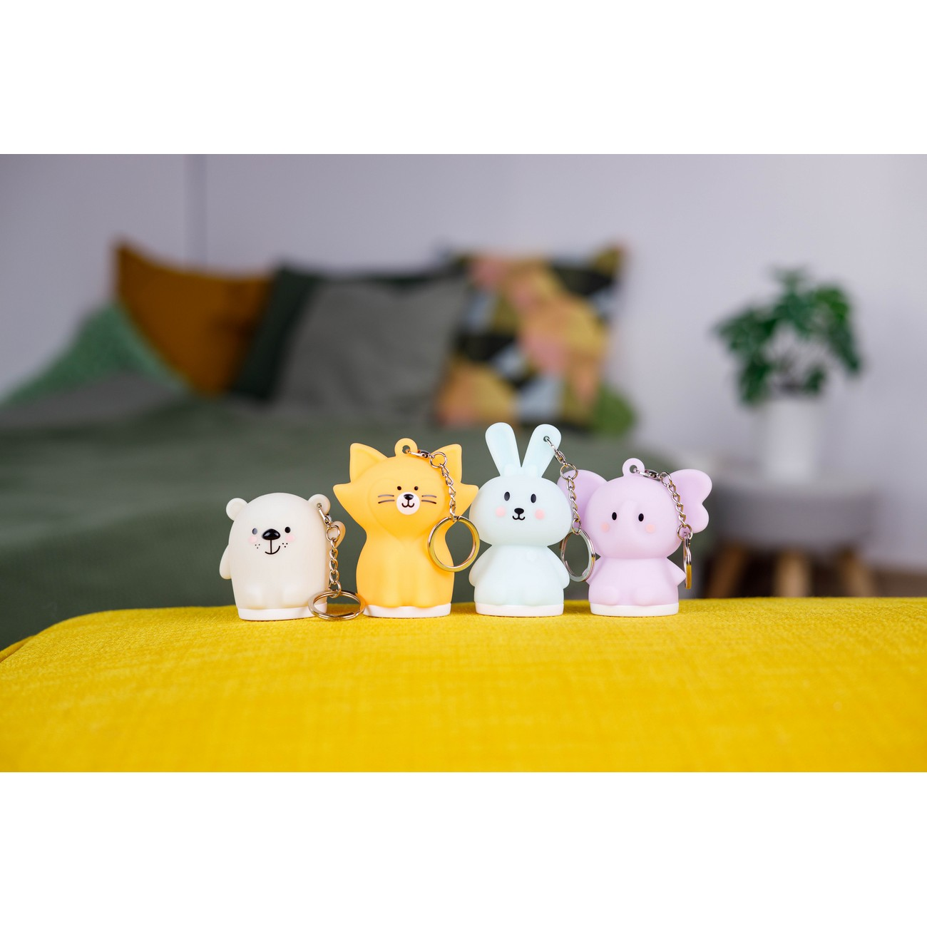 Cuatro llaveros de animales coloridos: oso, gato, conejo y elefante, sobre una superficie amarilla.