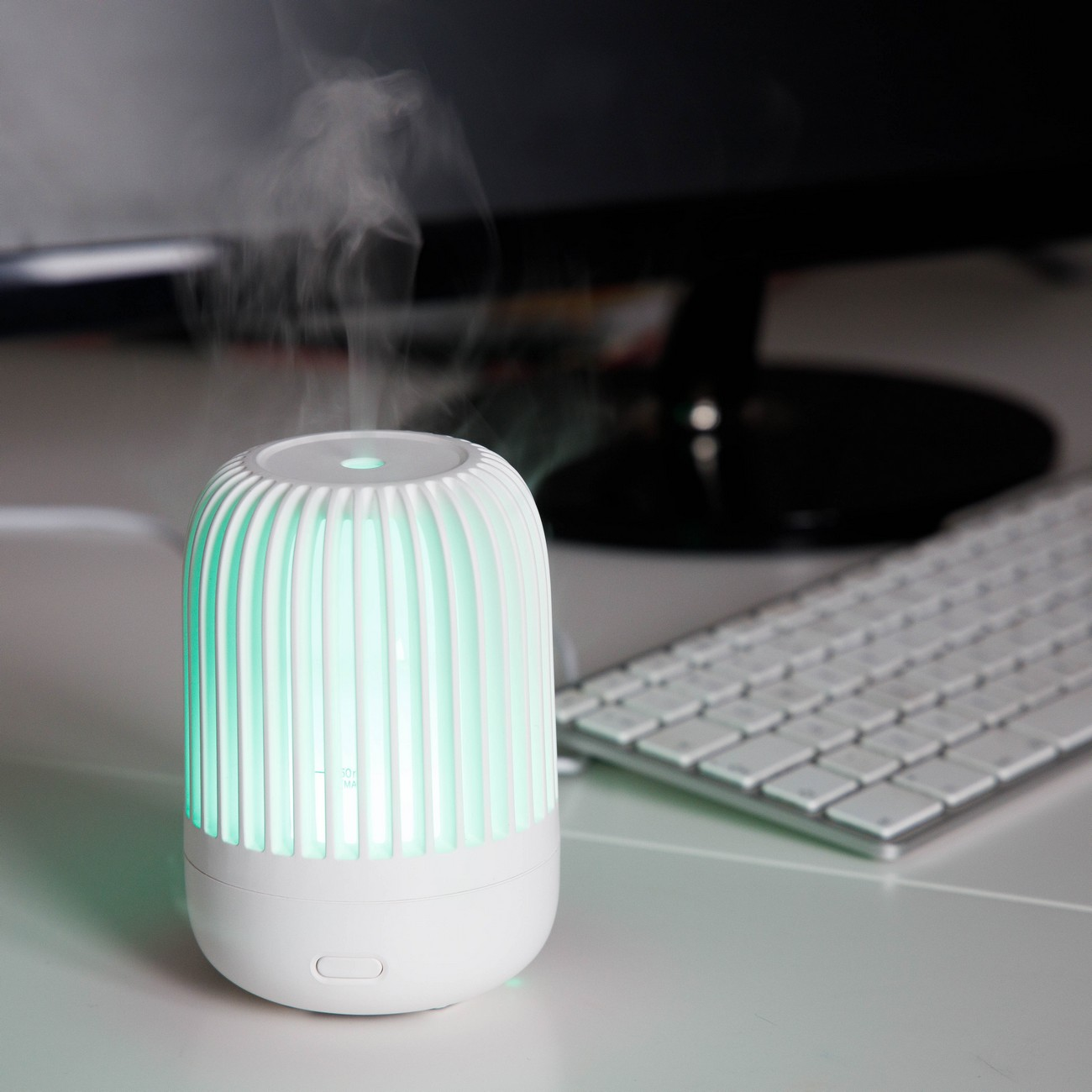 Humidificador blanco con luz verde emitiendo vapor. Un teclado está en el fondo.