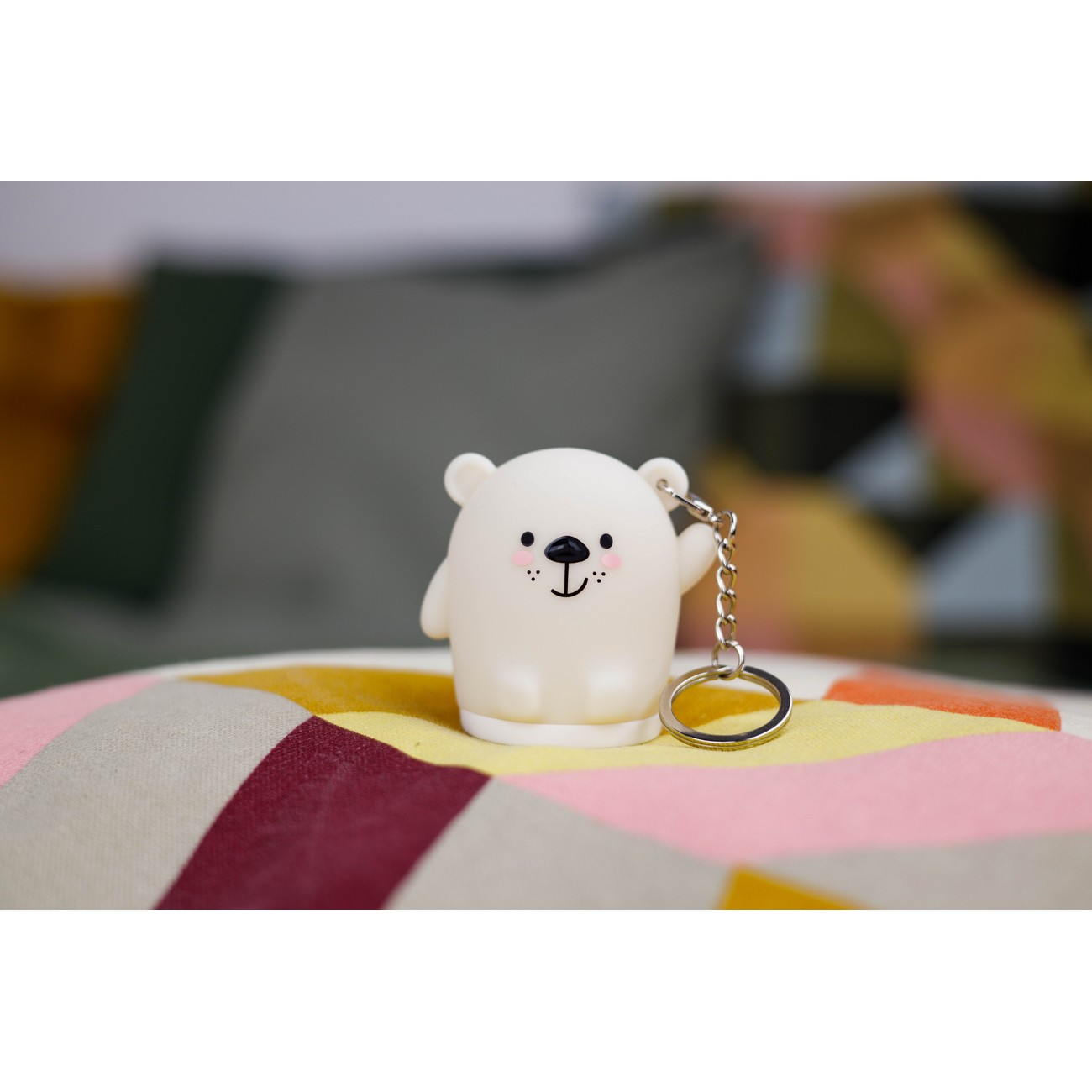 Llavero de oso blanco, sonriendo, con cadena. Sobre superficie colorida y estampada.