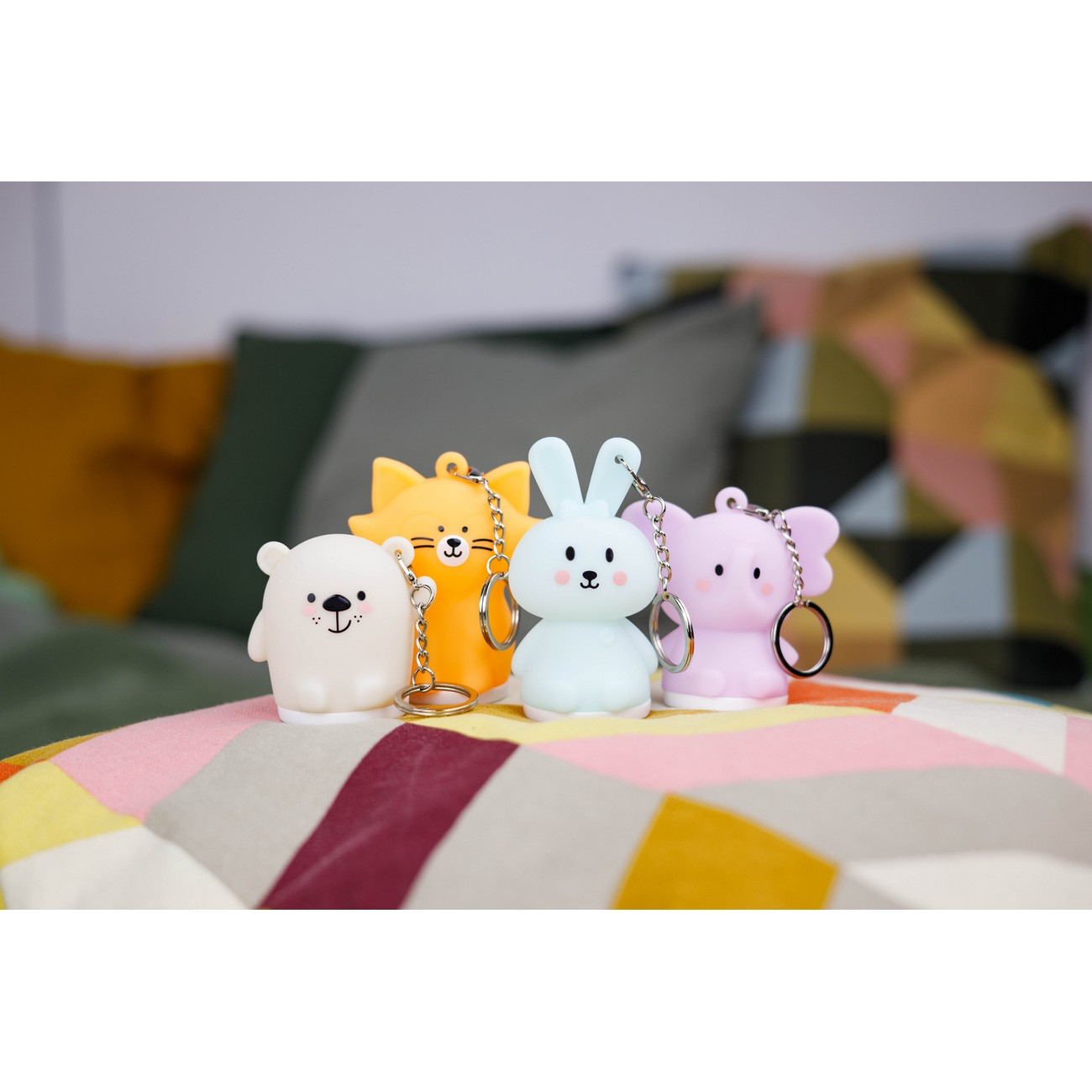 Cuatro llaveros de animales coloridos: oso, gato, conejito y elefante. Están sobre una superficie blanca y bien iluminados.