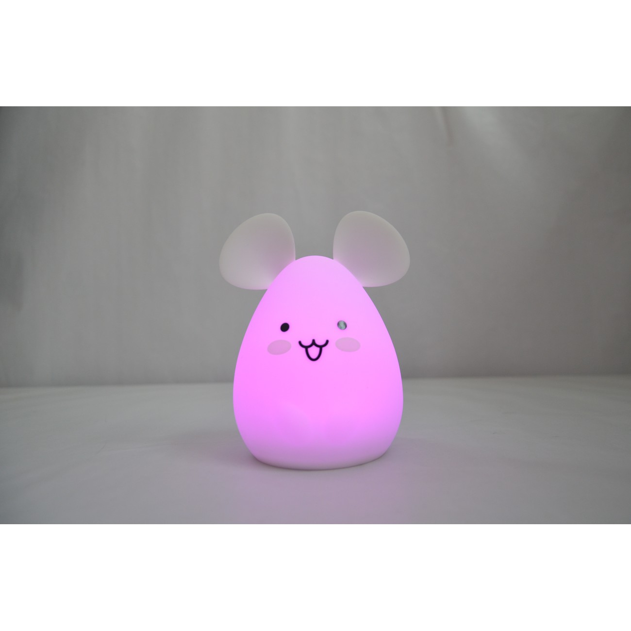 Luz nocturna rosa con forma de ratón, con dos orejas y una cara sonriente, sobre una superficie.