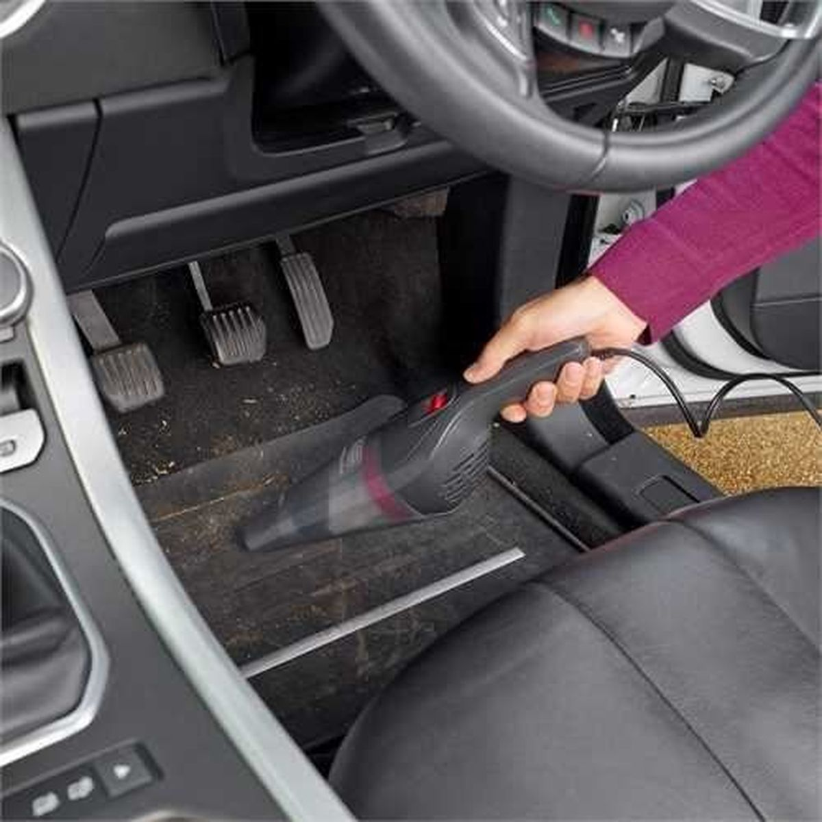Una persona che aspira l'interno di un'auto con un piccolo aspirapolvere portatile.