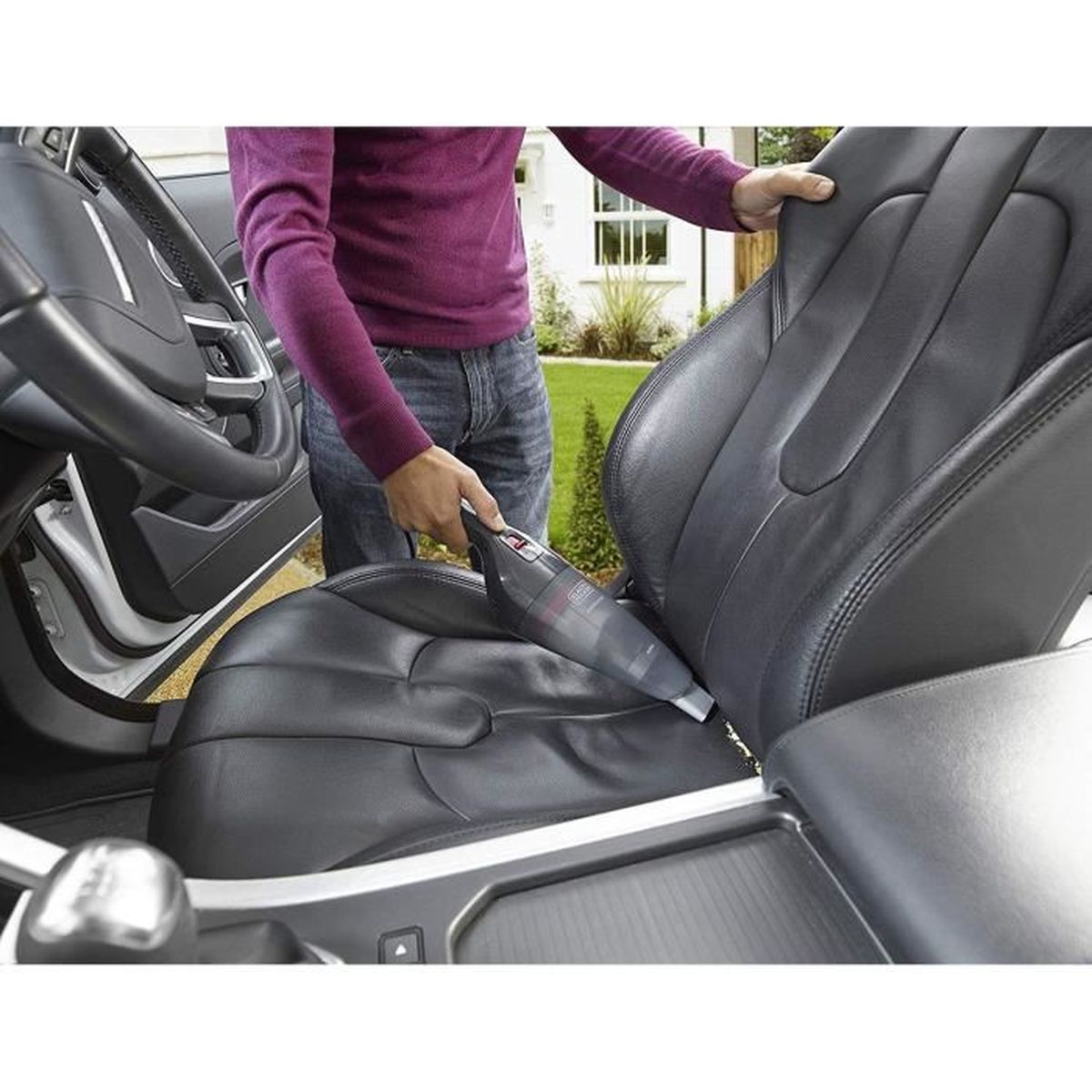 Persona che aspira il sedile dell'auto. Aspirapolvere portatile grigio, sedile in pelle nera. Interno auto.