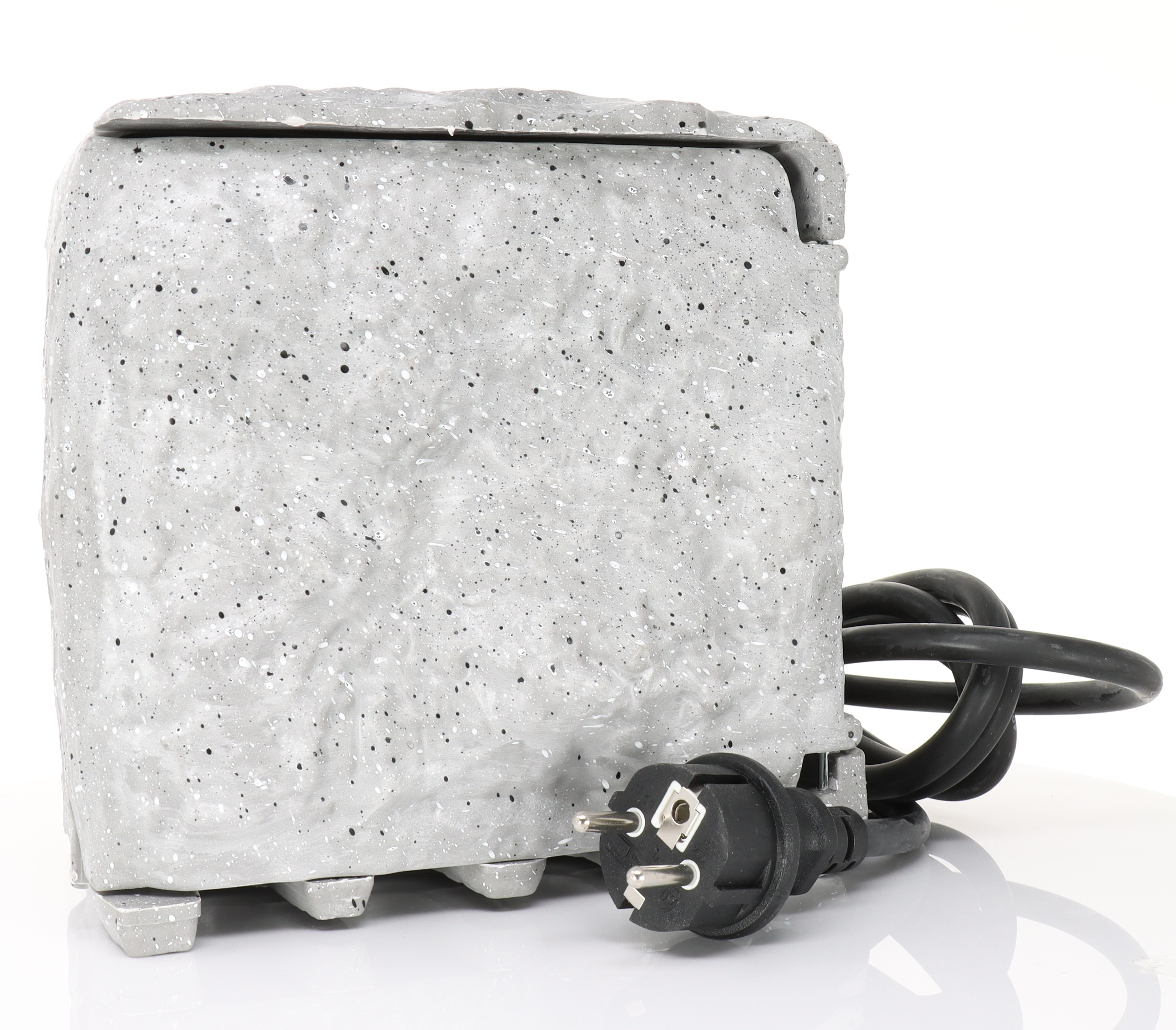 Ein grauer, gesprenkelter Betonblock mit Netzkabel. Der Stecker ist schwarz.