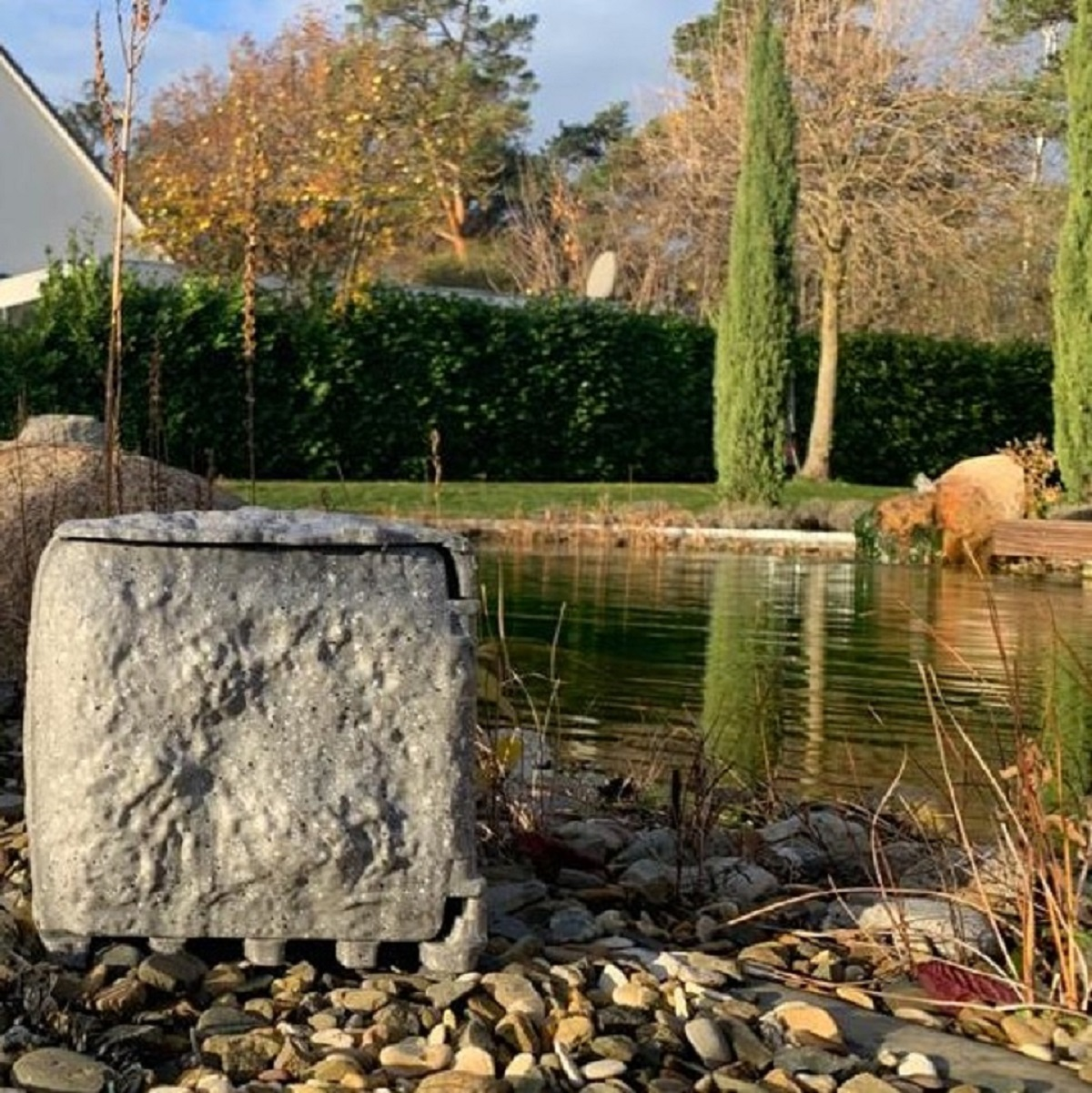 Eine Beton-Teichstruktur in natürlicher Umgebung mit Bäumen und Wasser.