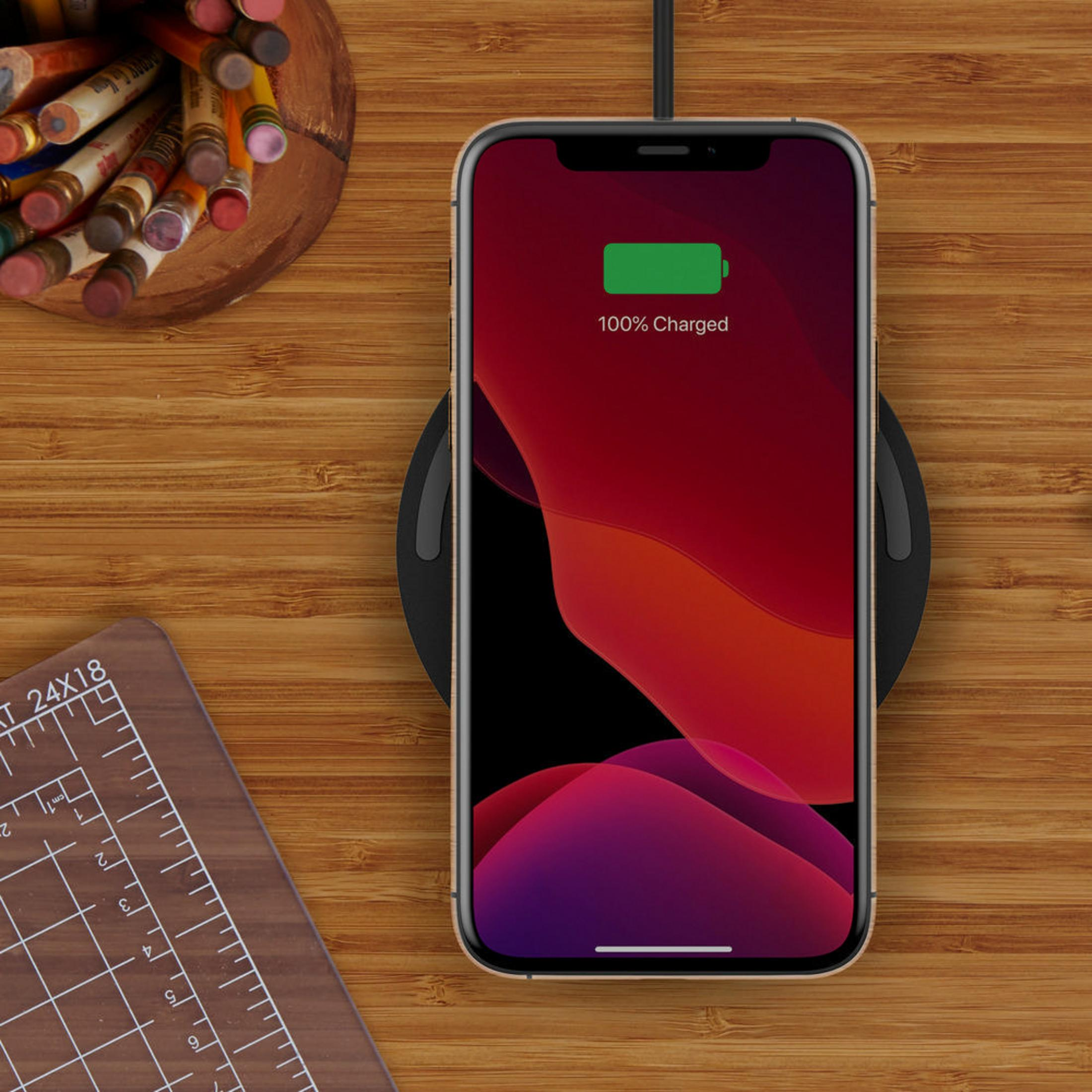 Ein Telefon liegt auf einem kabellosen Ladegerät und zeigt 100% geladen. Holzschreibtisch.