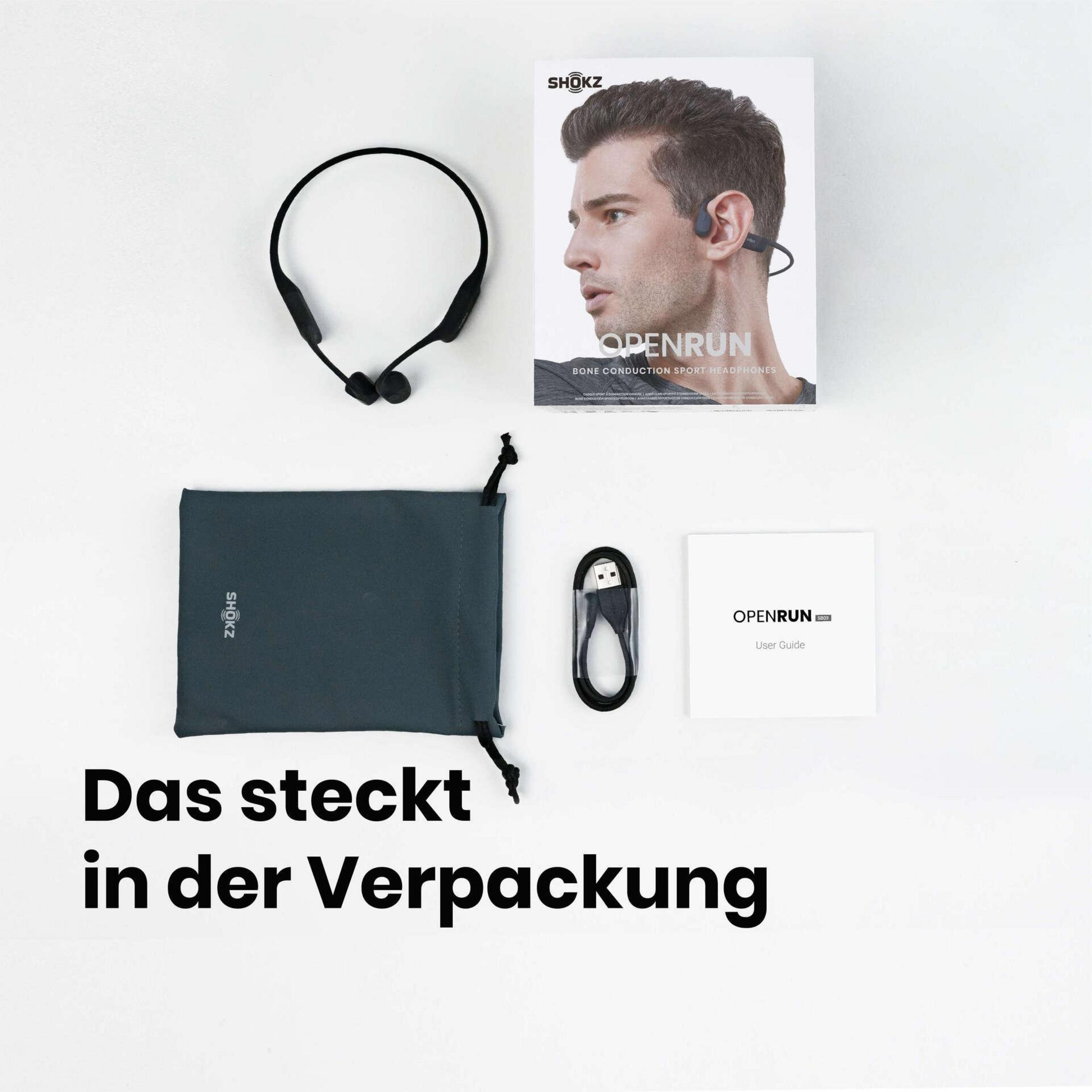 Draufsicht auf Shokz-Kopfhörer, eine Tragetasche, ein Ladekabel und eine Bedienungsanleitung auf weißer Oberfläche.