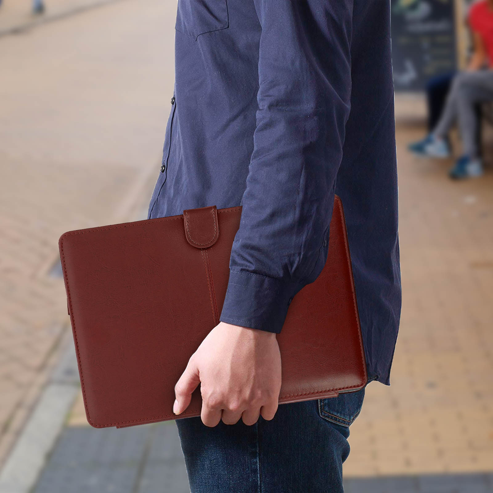 Uomo che tiene una custodia marrone per tablet mentre cammina per strada, sfondo sfocato.