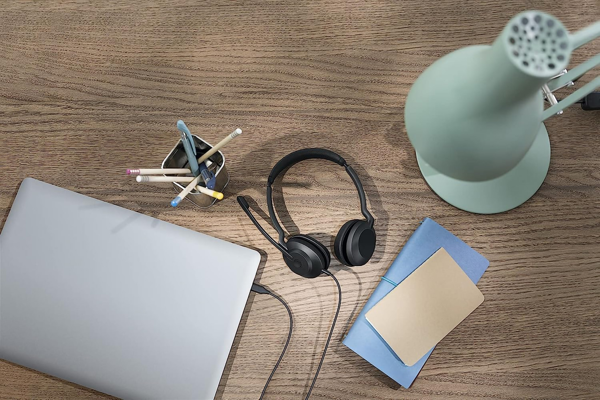 Schreibtisch mit Laptop, Headset, Stiften, Notizbuch und einer Schreibtischlampe.