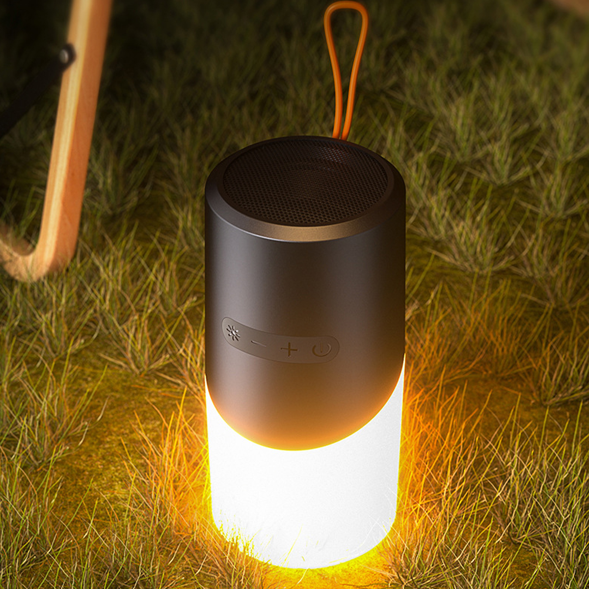 Un altavoz portátil negro y naranja está sobre la hierba. Brilla con una luz cálida y anaranjada.