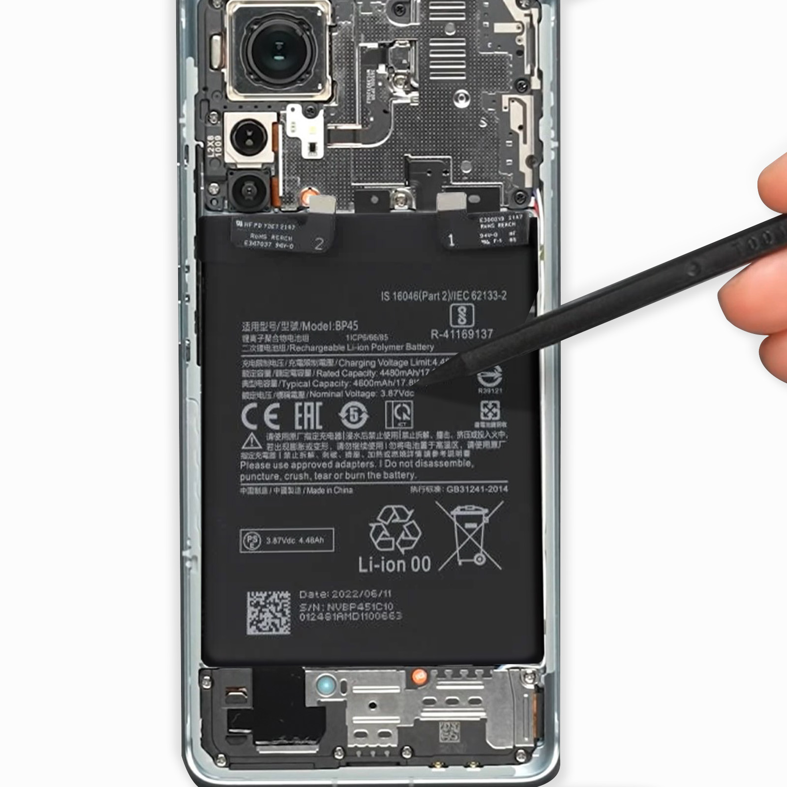 Composants internes du téléphone visibles, y compris la batterie, la carte et l'appareil photo. Un outil est à proximité.