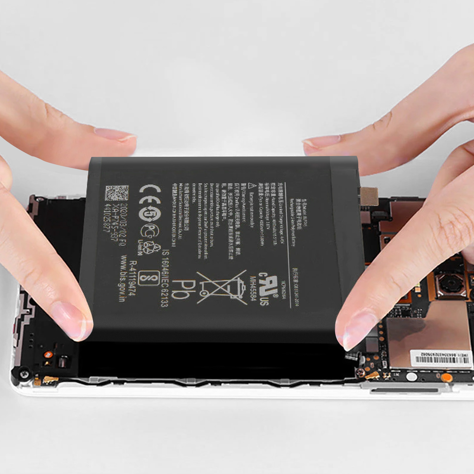 Hände halten einen Telefonakku über einem geöffneten Telefon, dessen innere Komponenten sichtbar sind.