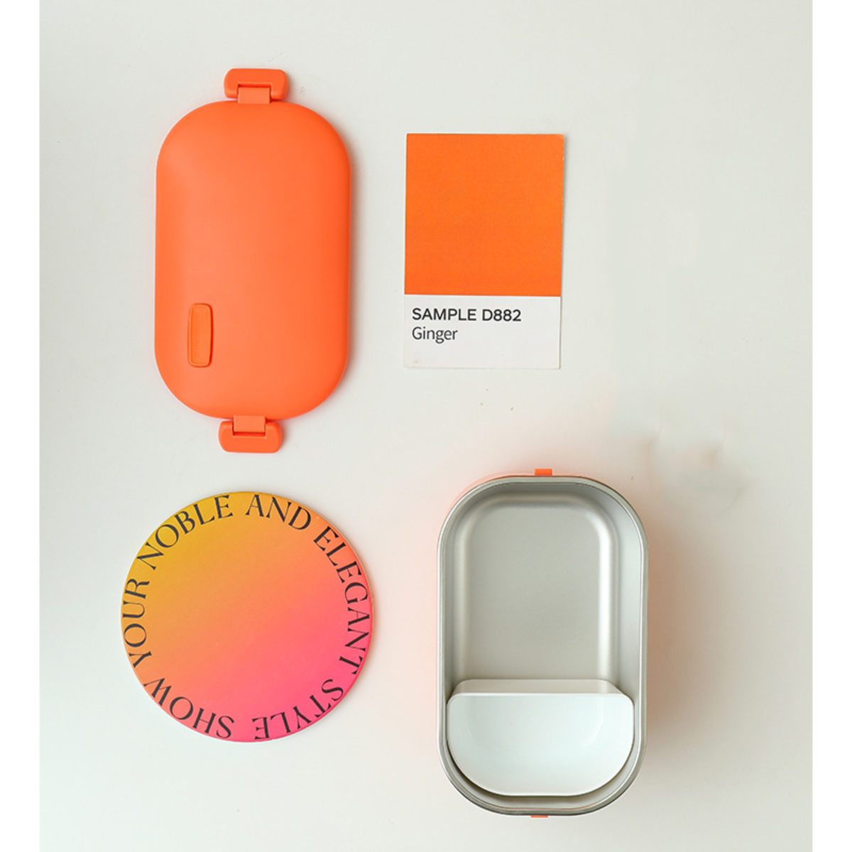Accesorios naranjas sobre una superficie blanca. Incluye una funda, una muestra de color con 'Ginger' y un diseño redondo.