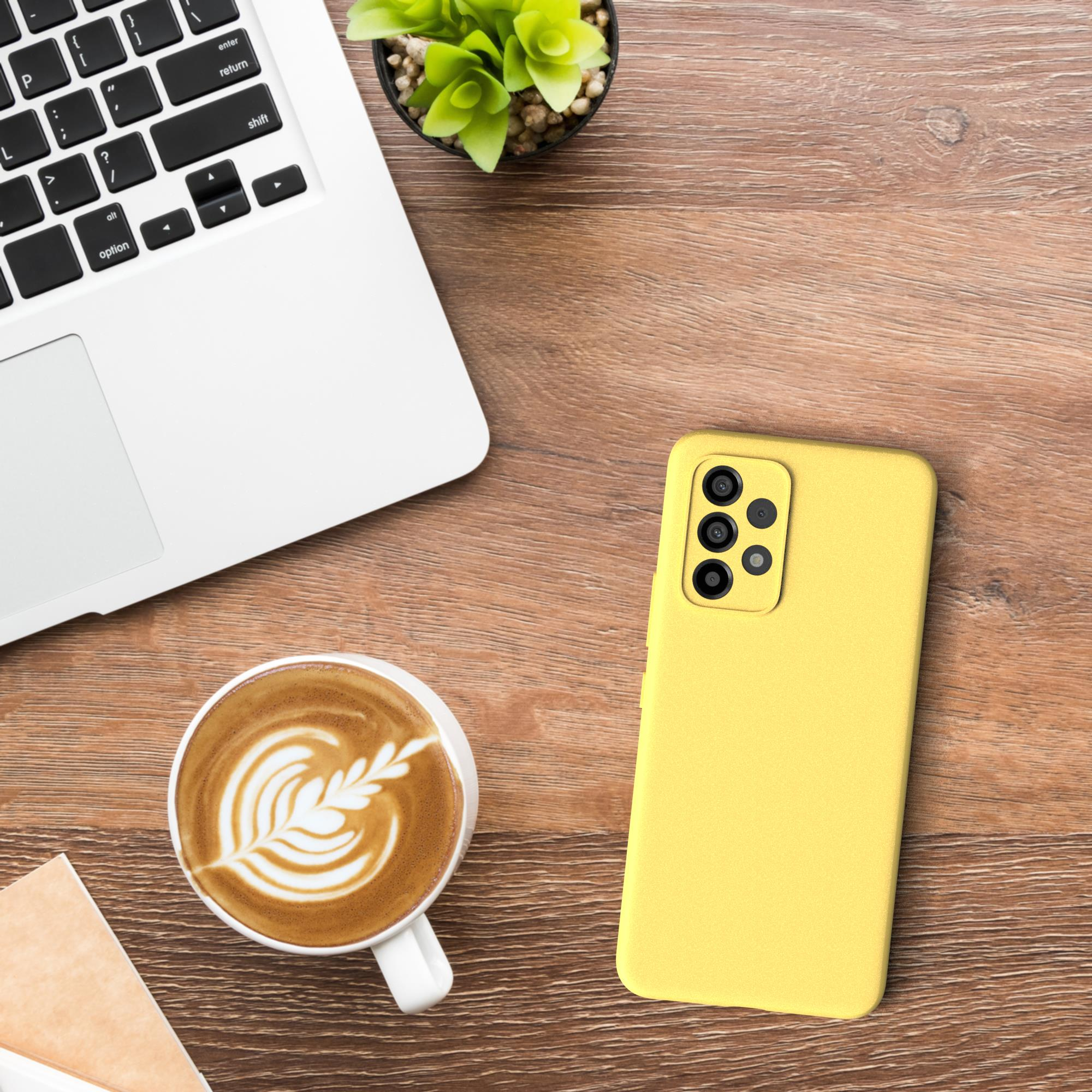 Eine gelbe Handyhülle auf einem Holzschreibtisch, mit einer Kaffeetasse, einem Laptop und einer kleinen Pflanze im Hintergrund.