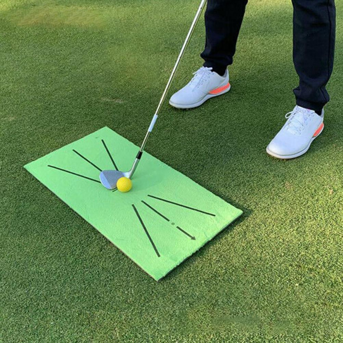 Eine Person, die auf einer grünen Matte mit Golfschläger und Ball Golf spielt. Der Hintergrund ist Gras.