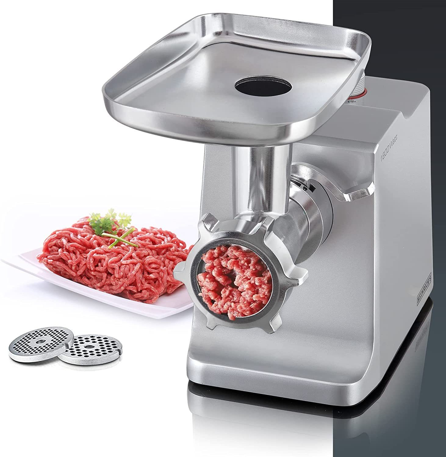 Ein silberner Fleischwolf mit Hackfleisch vorne und einem Teller Fleisch hinten.