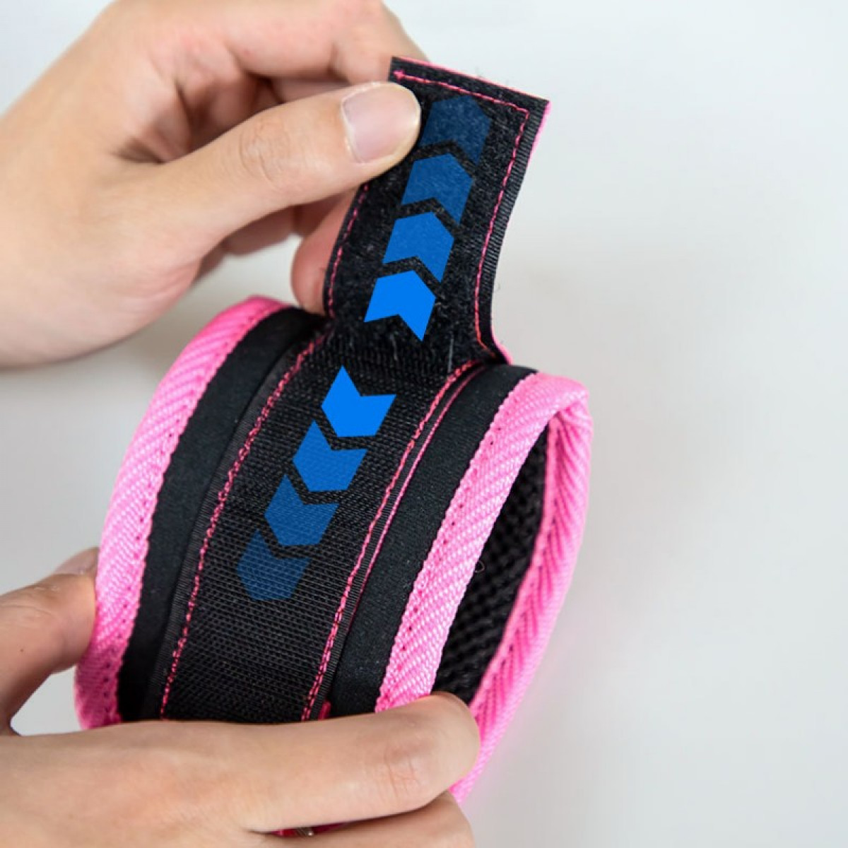 Dłonie rozciągają różowo-czarną opaskę na nadgarstek z niebieską strzałką.