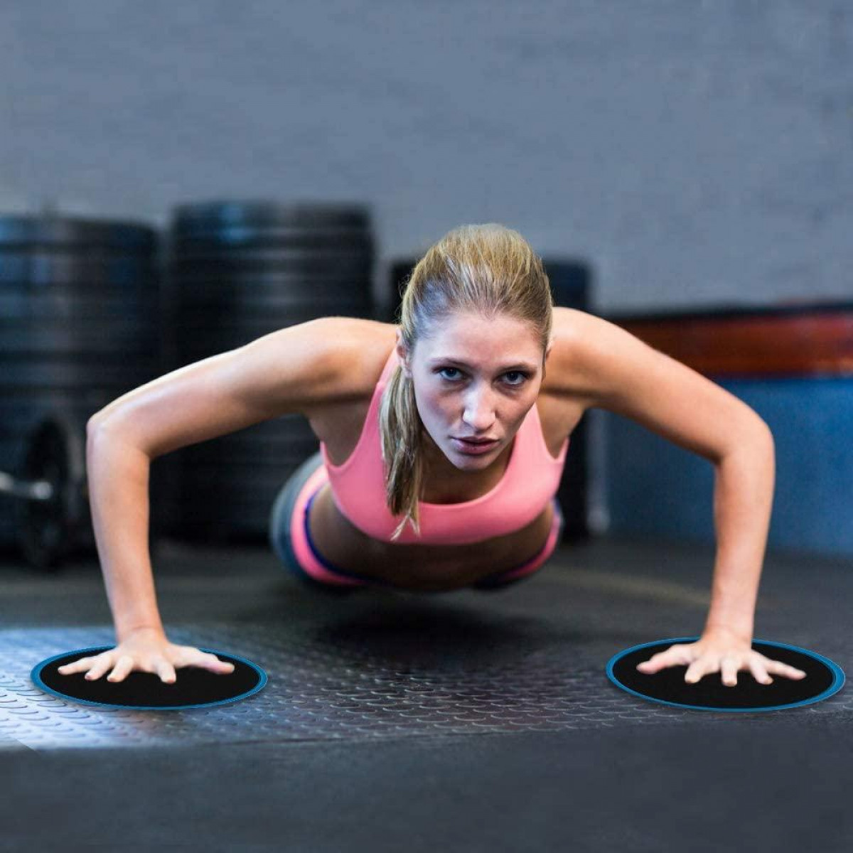 Frau macht Liegestütze auf einem Fitnessstudioboden. Zwei schwarze und blaue Scheiben unter ihren Händen.