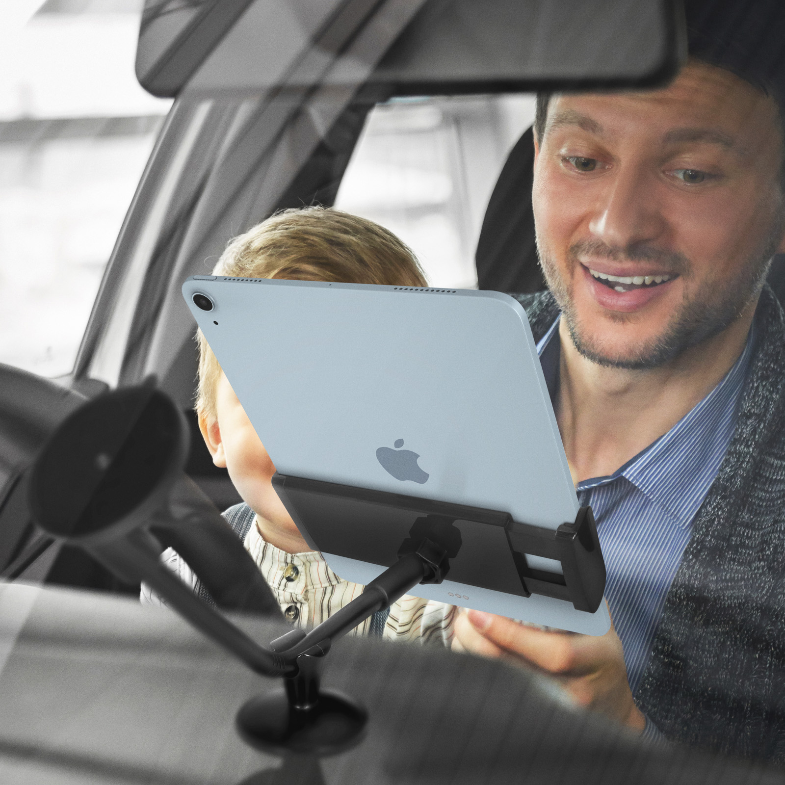 Mann und Kind im Auto schauen auf ein Tablet, das an einem Halter befestigt ist.