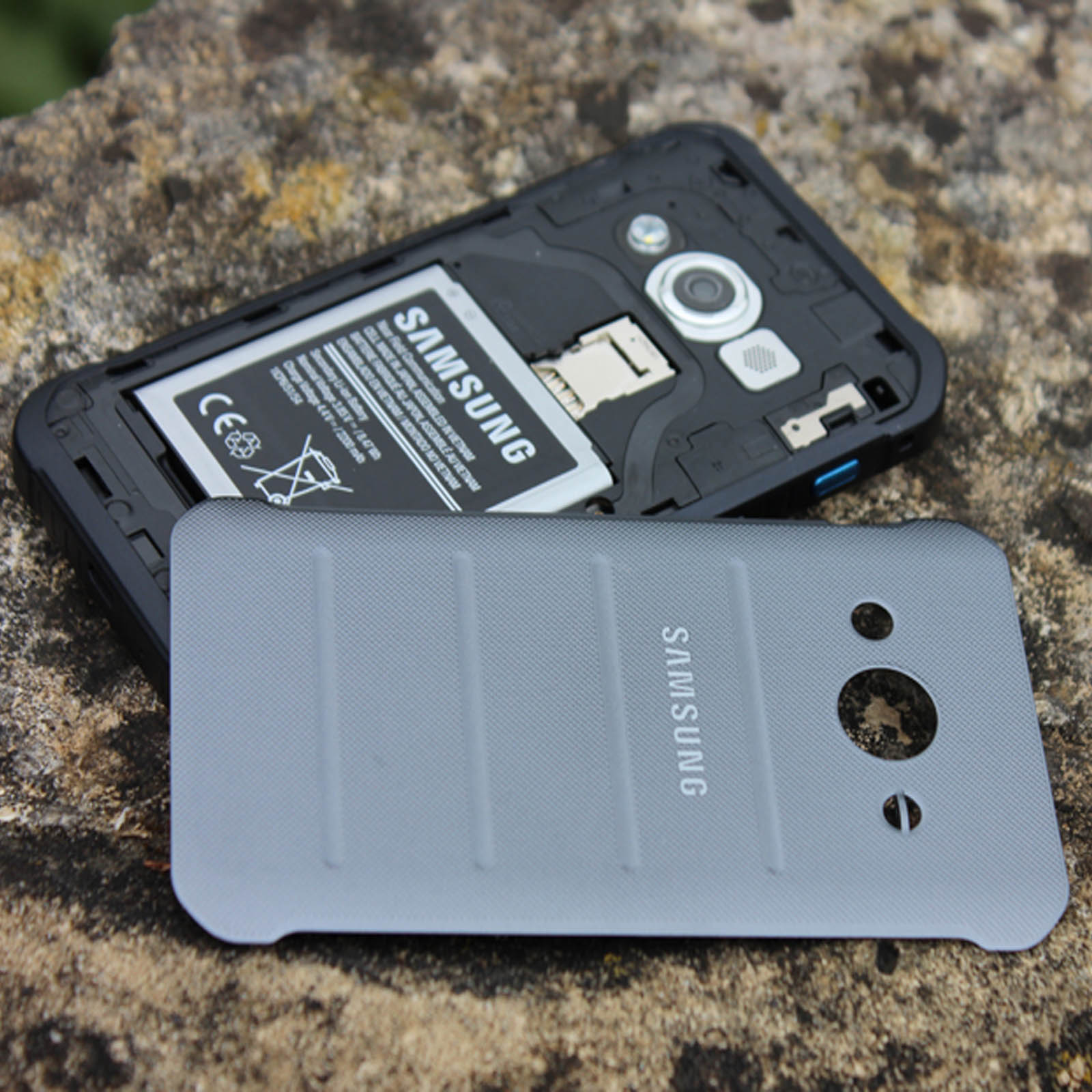 Componenti del telefono su pietra. Batteria, cover posteriore e telaio del telefono. Logo Samsung visibile.