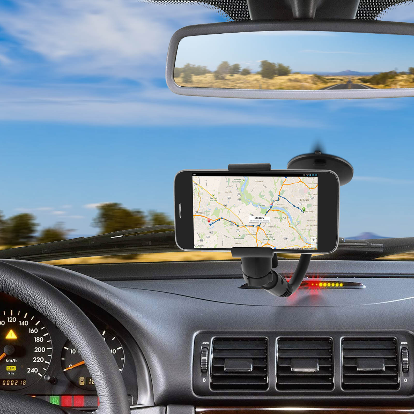 Telefonhalterung auf dem Armaturenbrett eines Autos mit Karte. Himmel und Straße sichtbar.